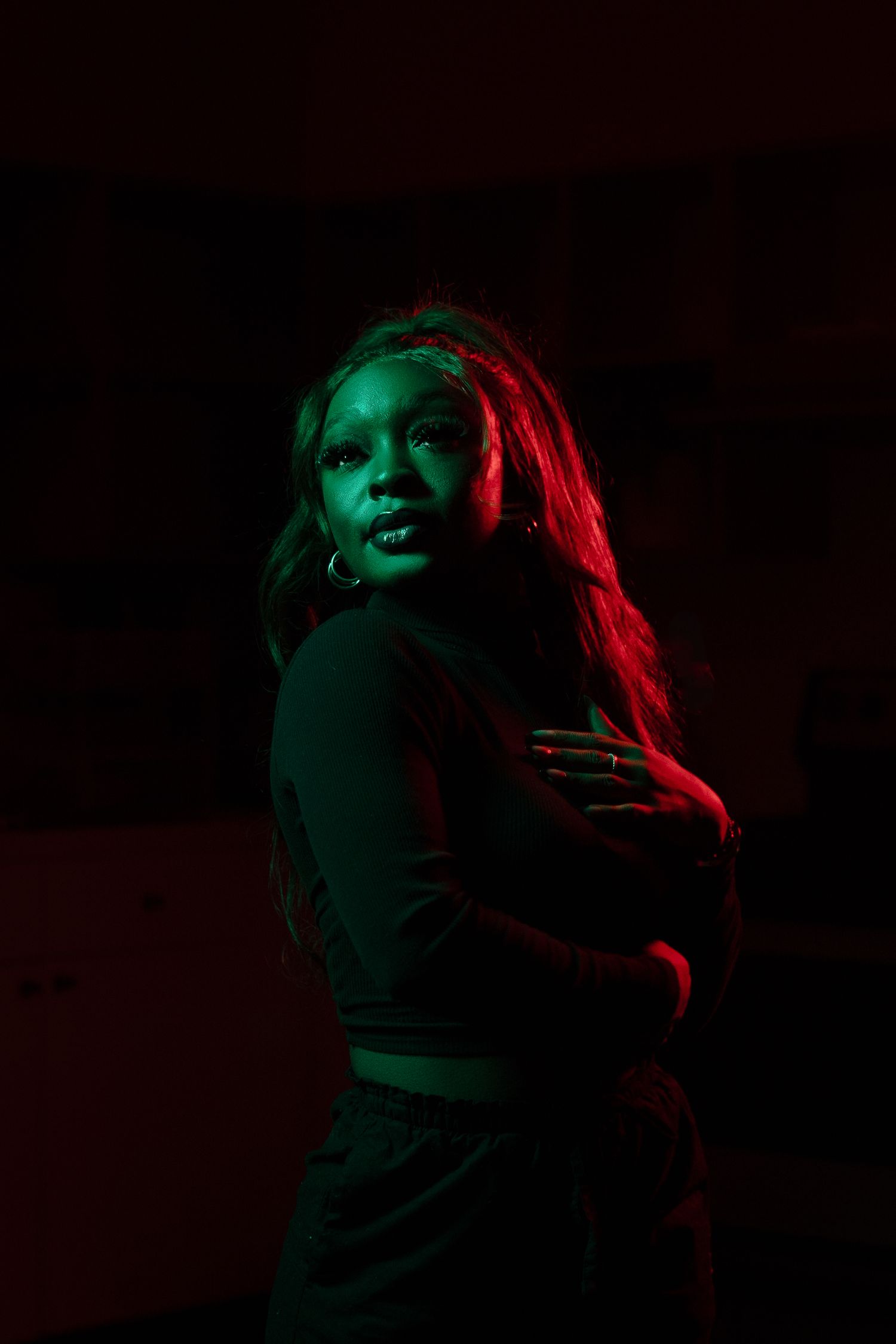 Artistic portrait with dramatic red and green lighting creating moody atmosphere in dark setting.