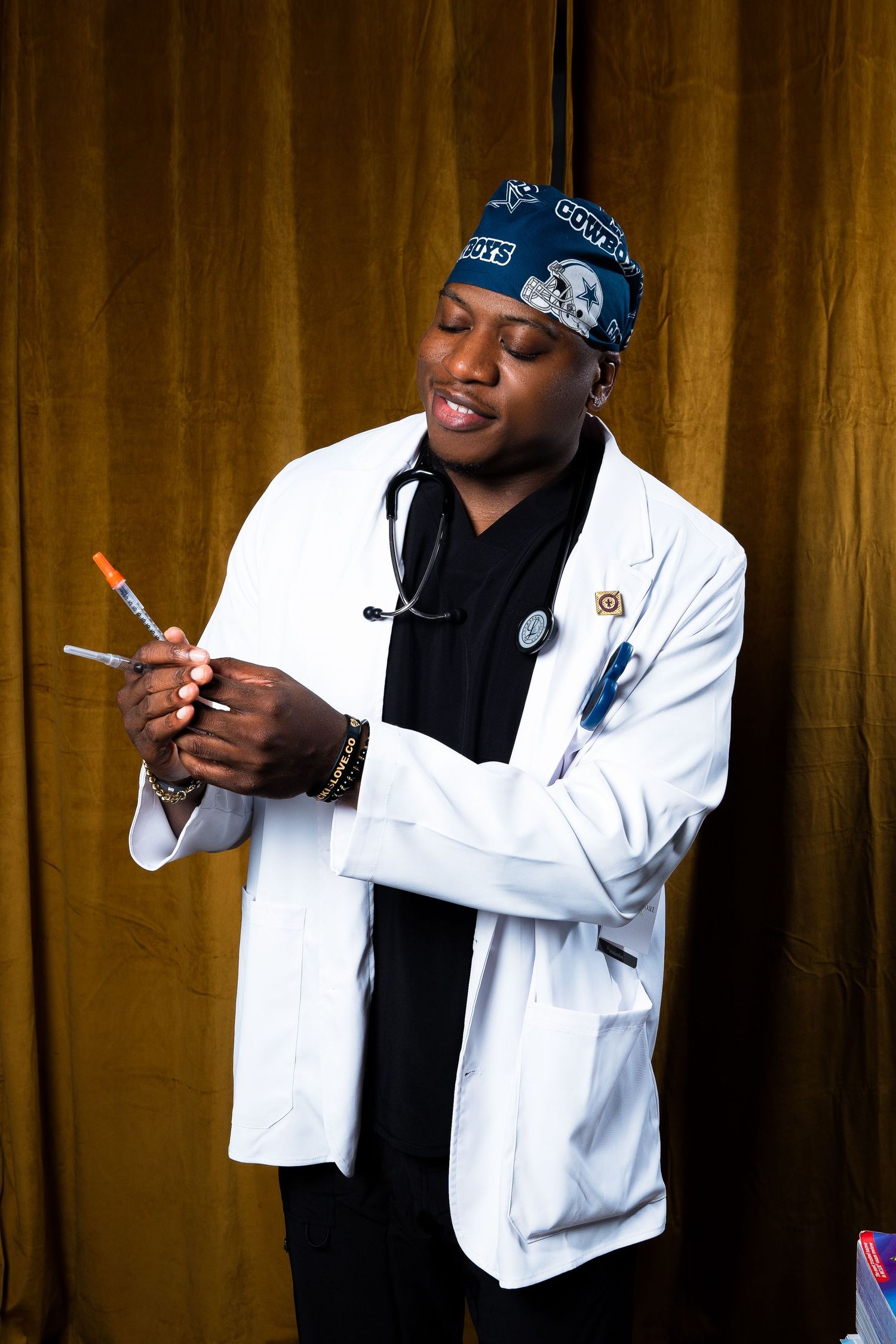 Model in white lab coat and baseball cap poses playfully against gold backdrop.