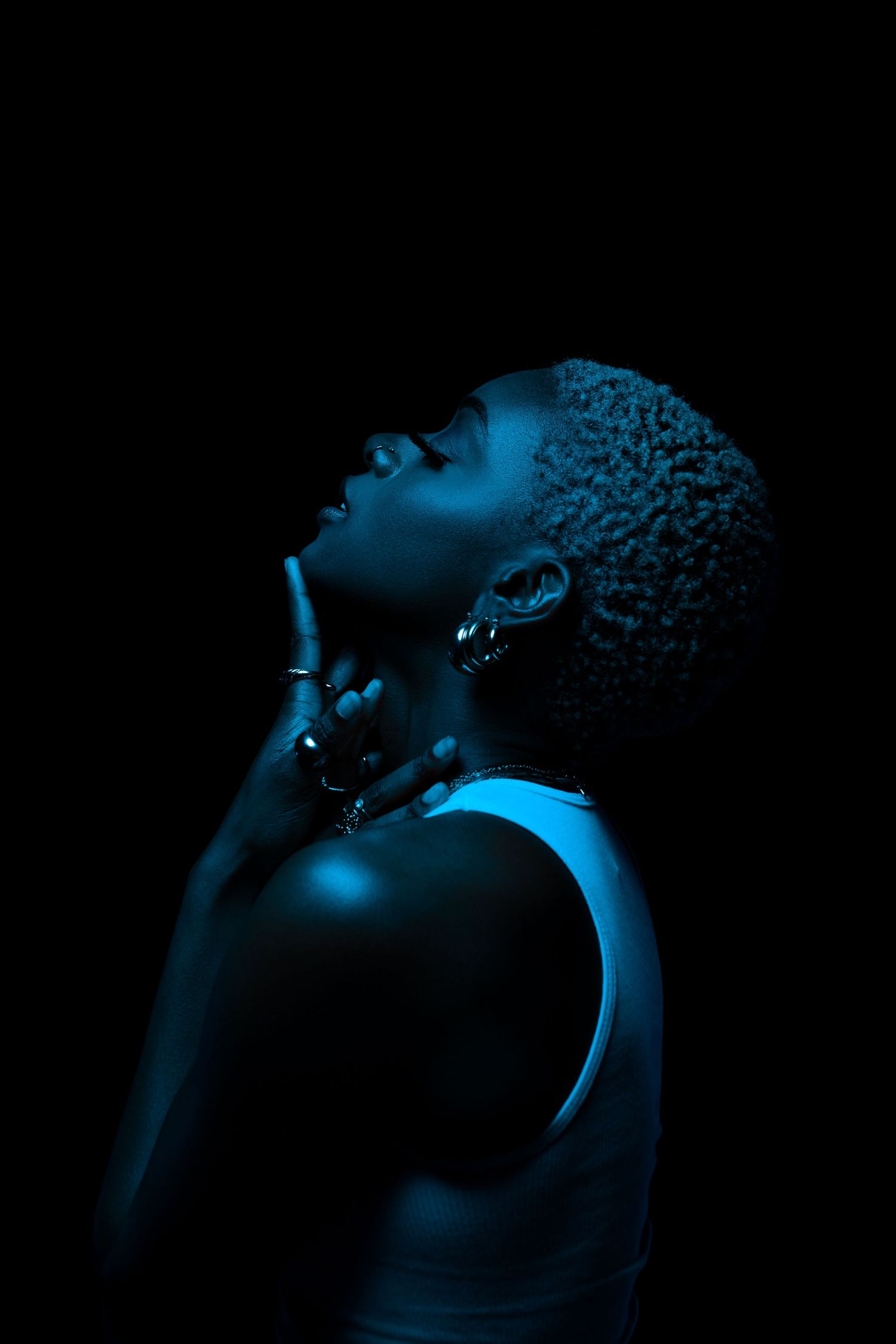 Profile view of person bathed in blue light against black background.