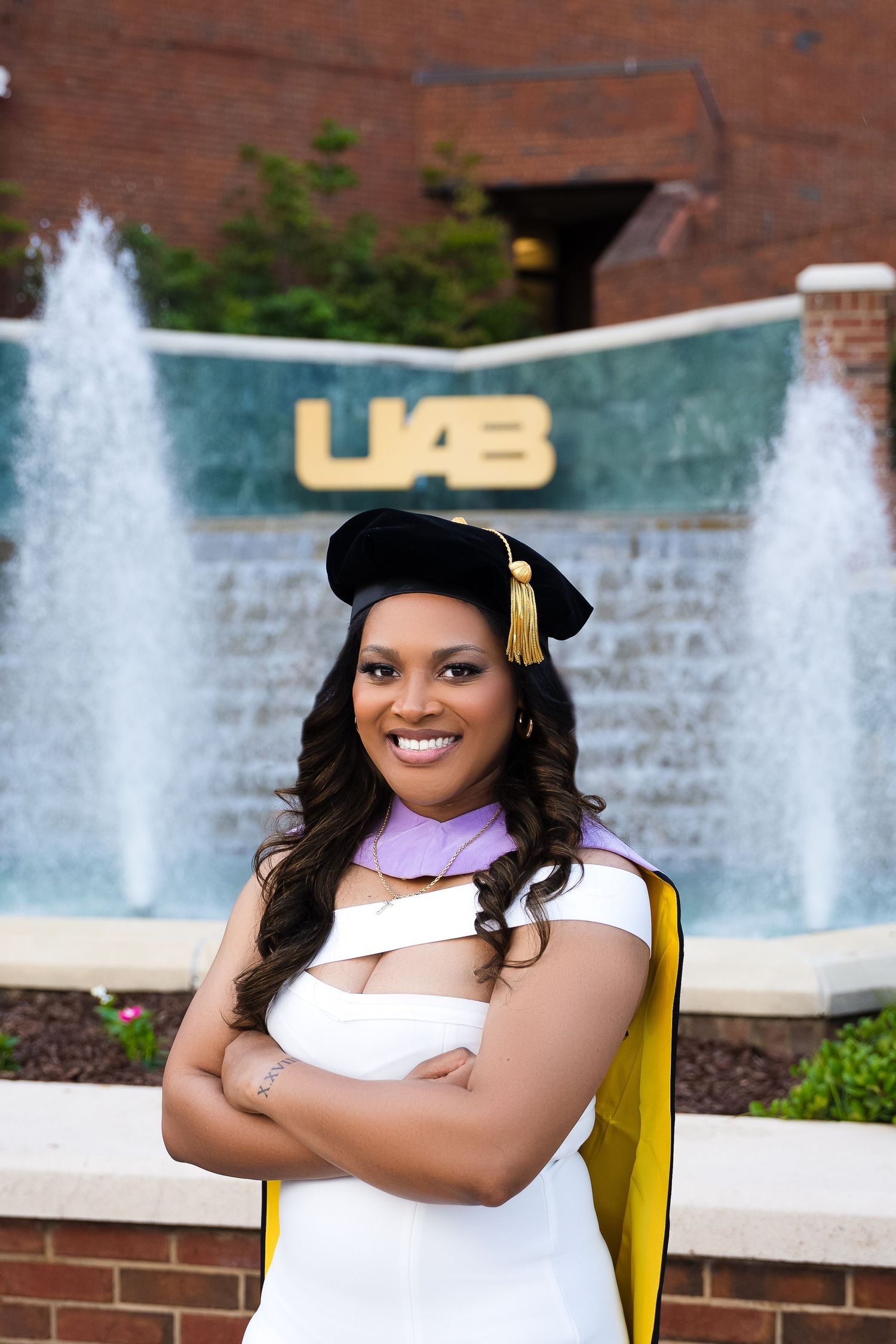 Graduate poses in front of UAB fountain wearing academic regalia and tassel cap.