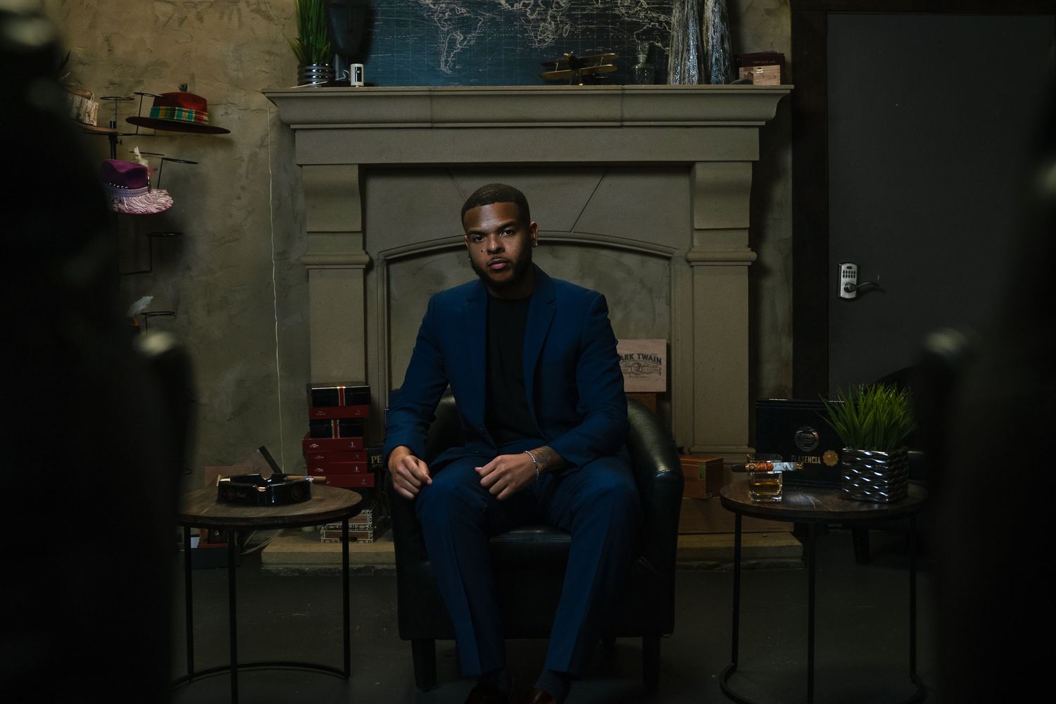 Professional portrait in navy suit seated by ornate fireplace in moody lighting.