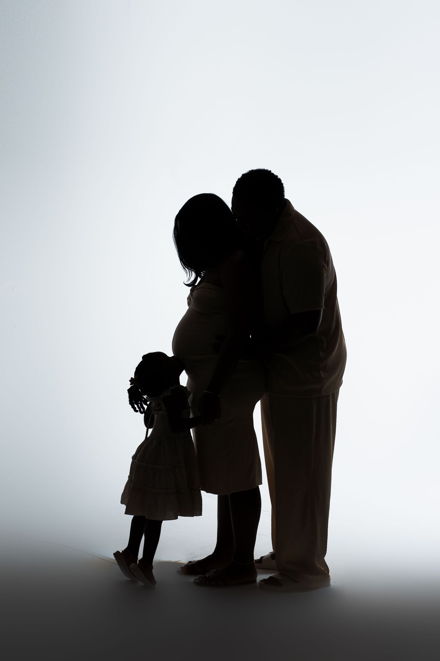 A silhouette portrait of a family standing together against a light background.