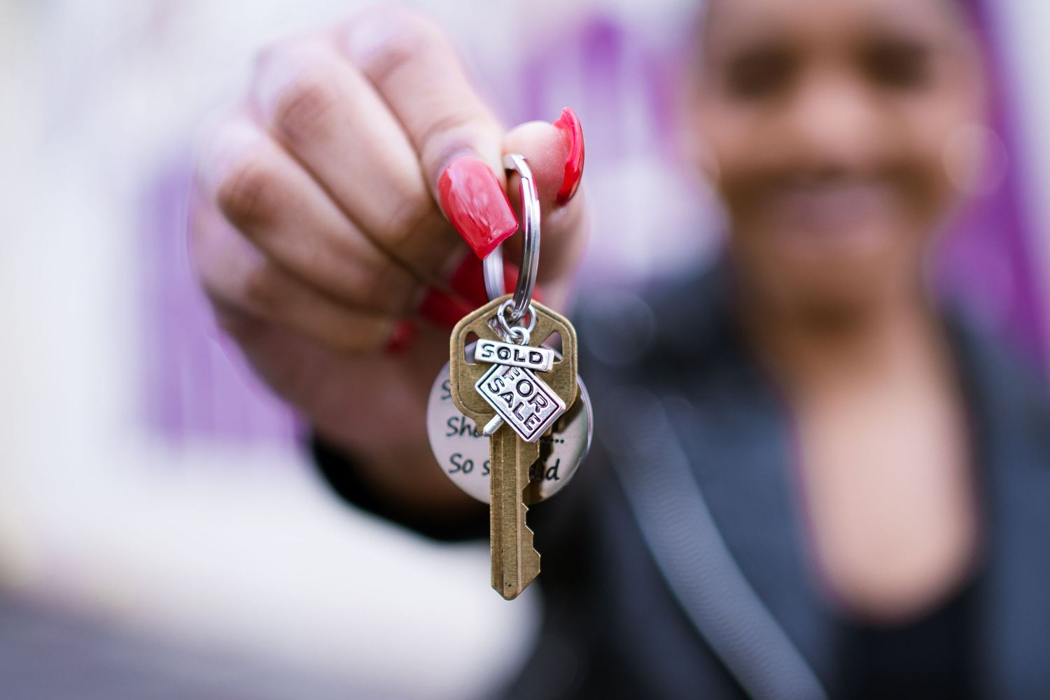 Close-up of hand holding house key with decorative keychain.