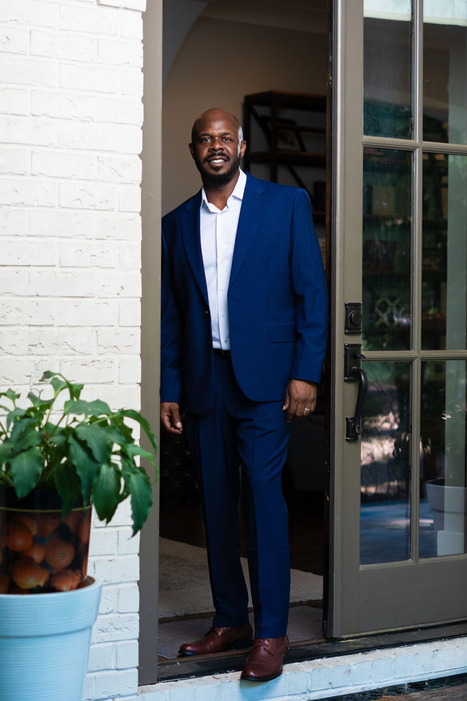 Professional portrait in navy suit standing in doorway with potted plant.