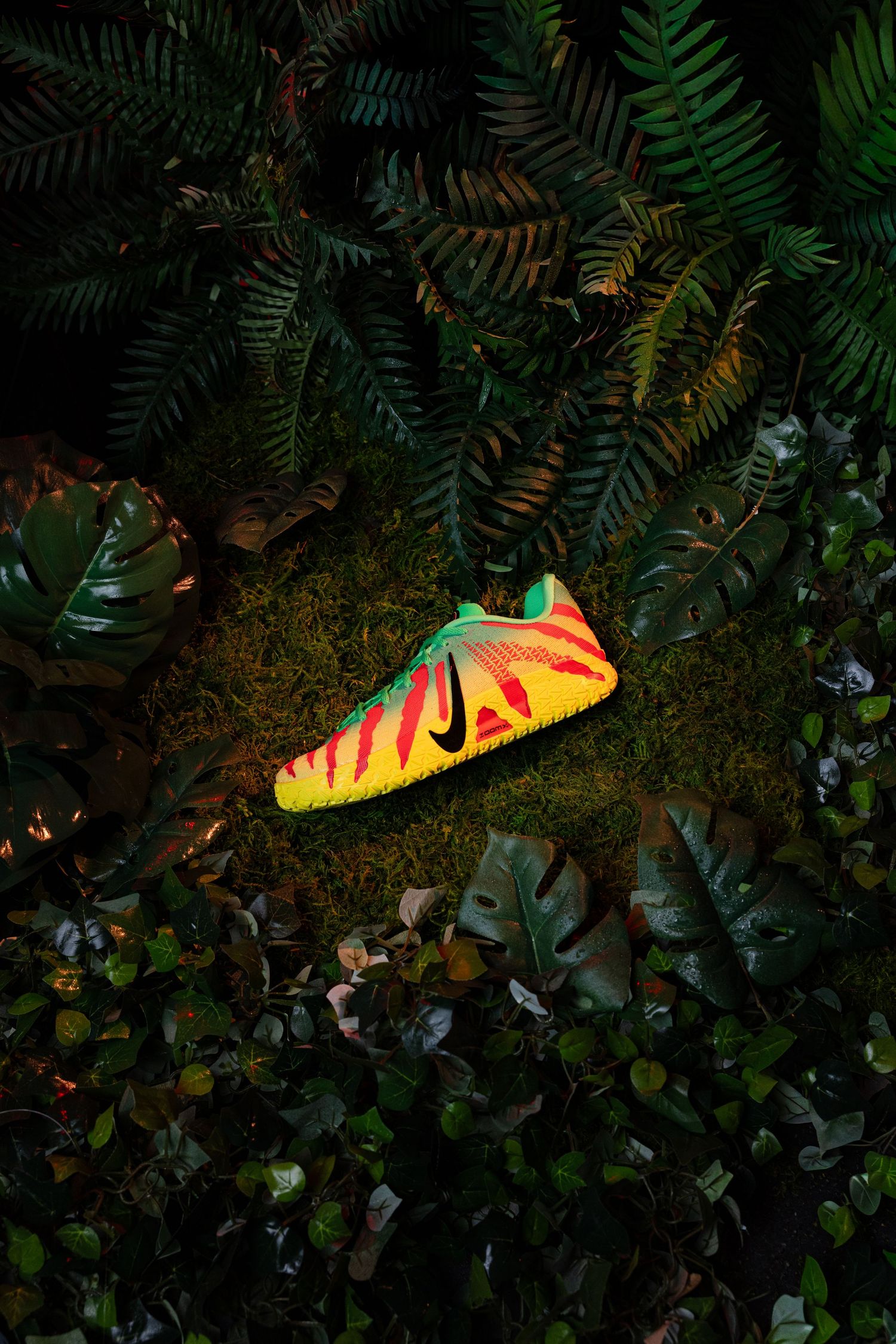 Vibrant yellow and red Nike sneaker resting on moss surrounded by lush tropical ferns and monstera leaves.