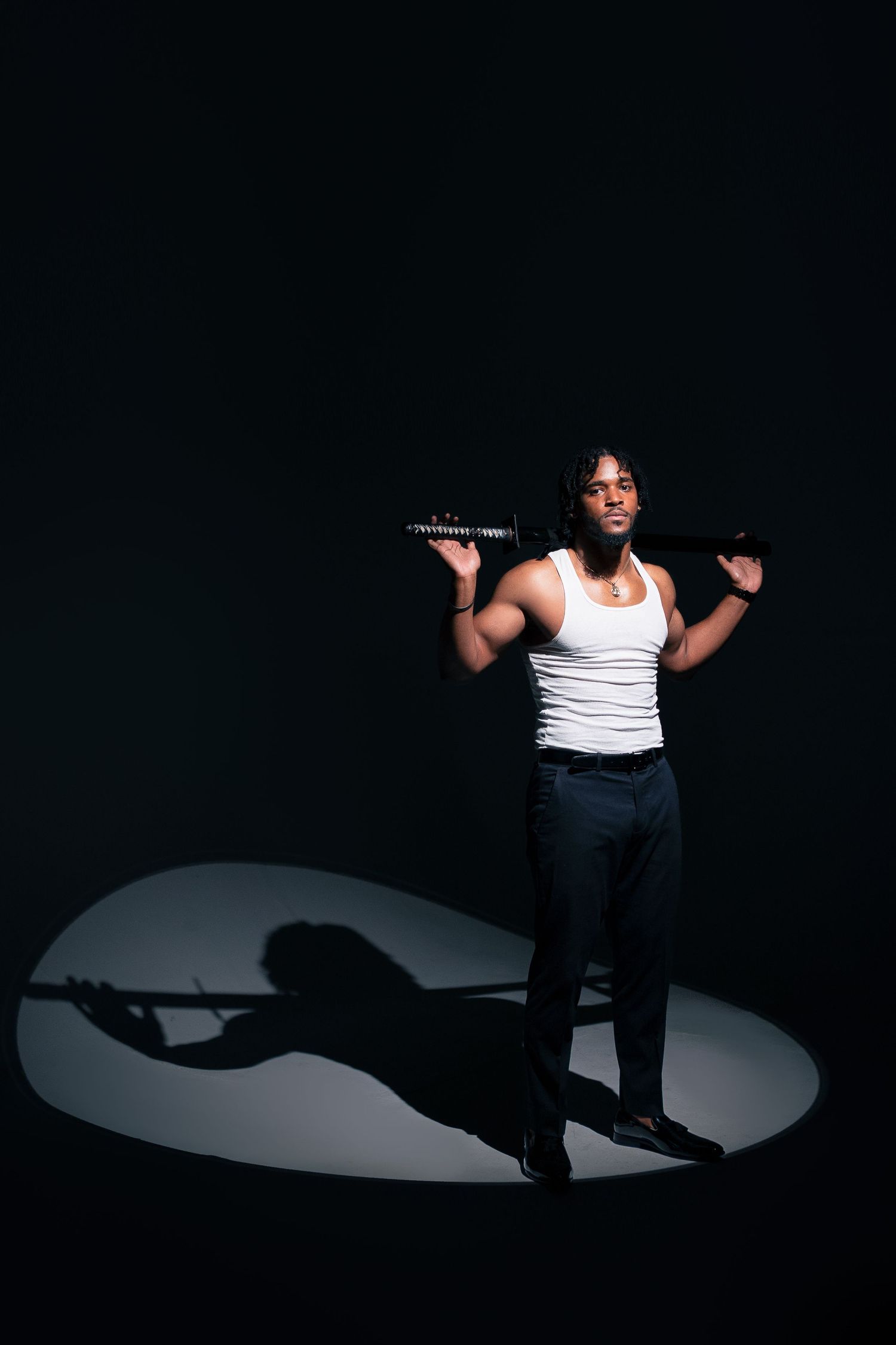 Dramatic spotlight illuminates person in white tank top holding dumbbells on dark background.