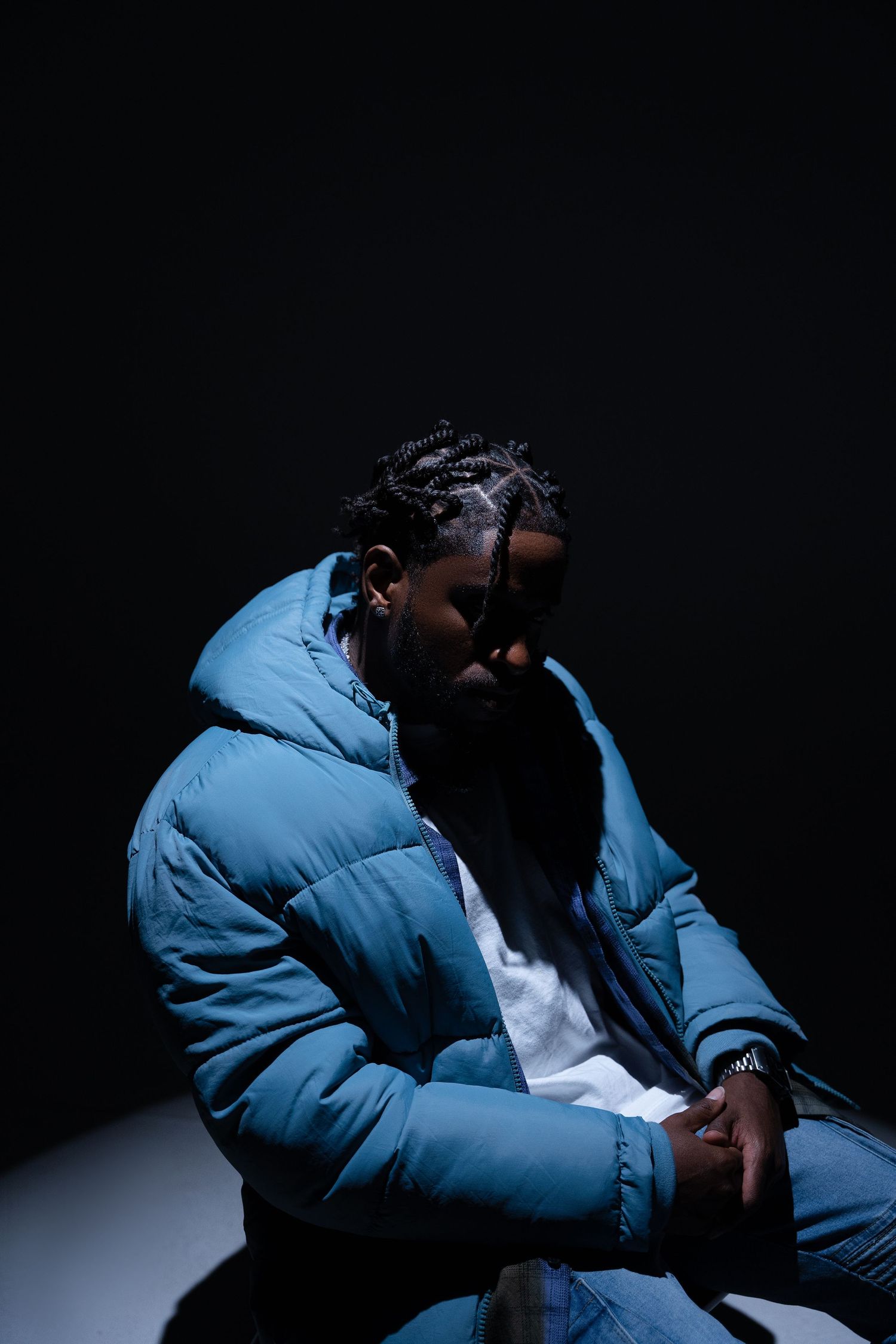 Moody portrait of person in blue puffer jacket against dark background.