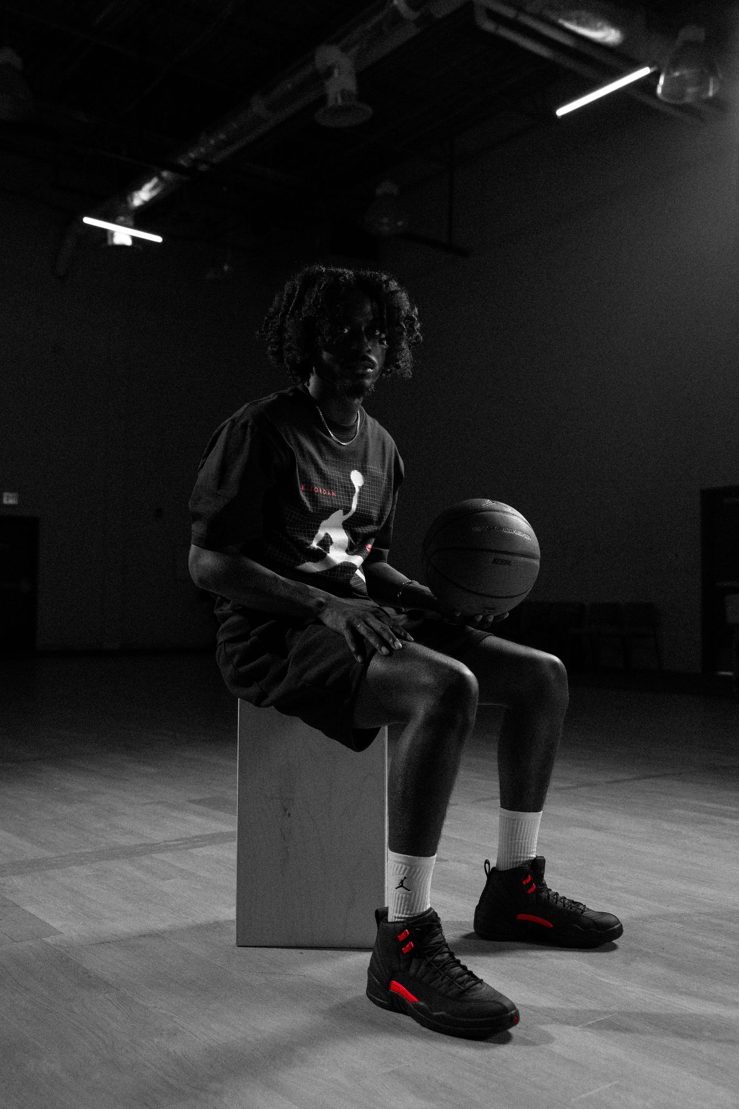 Young basketball player in Jordan Brand apparel sits on a box with a basketball in a dark gym.