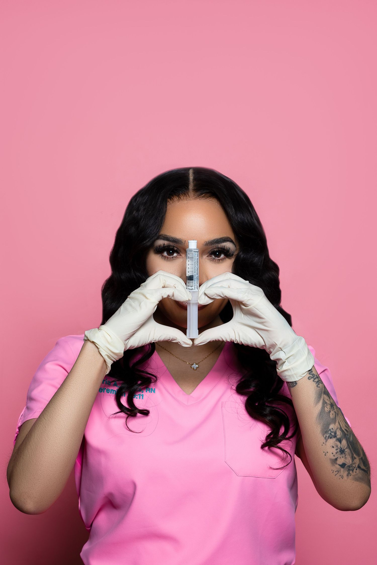 Healthcare worker in pink scrubs holding syringe against pink background.
