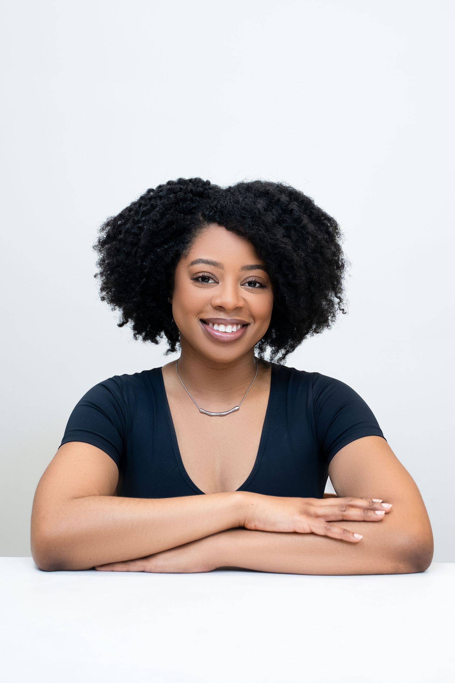 Professional headshot with natural curly hair against white background.
