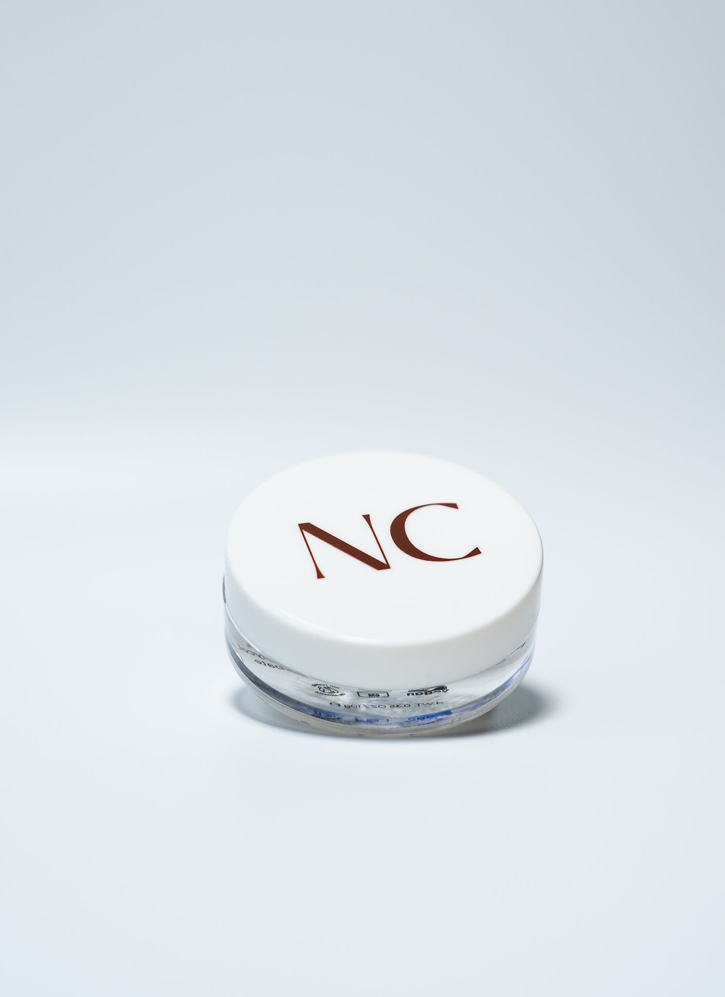 White cosmetic jar with NC logo branding on light gray background.