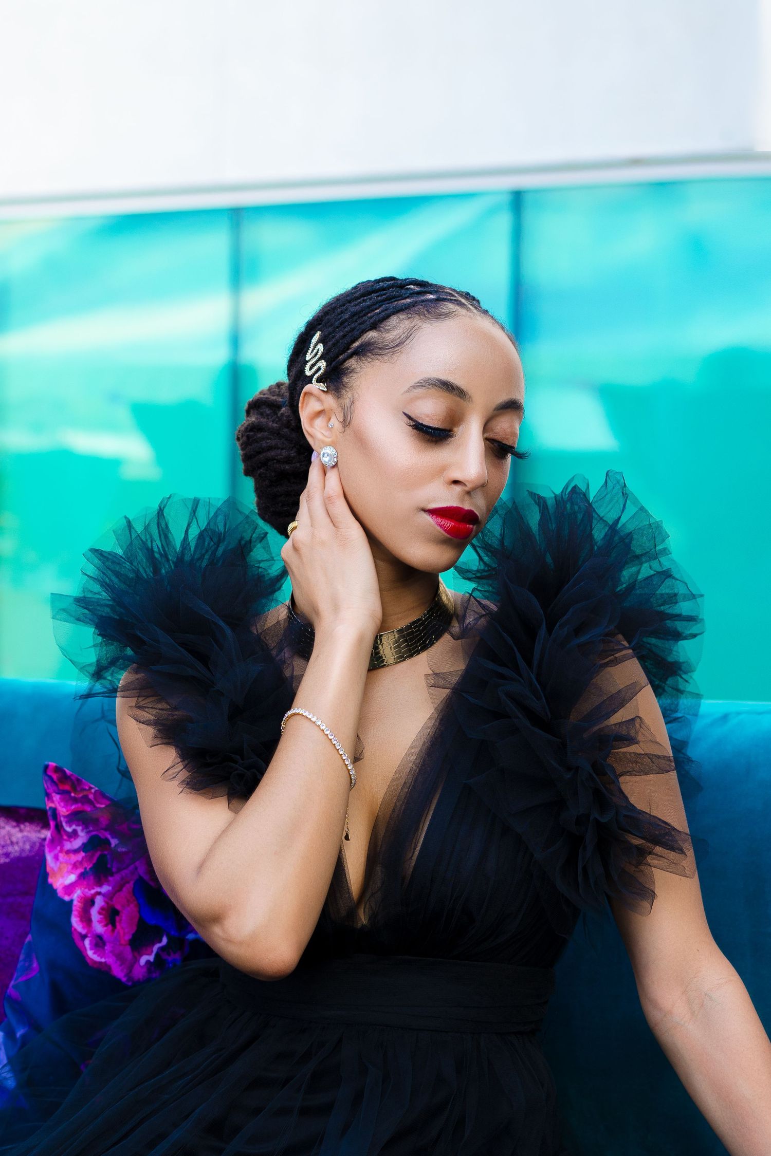 A glamorous portrait featuring a black tulle dress with dramatic shoulders against a turquoise background.