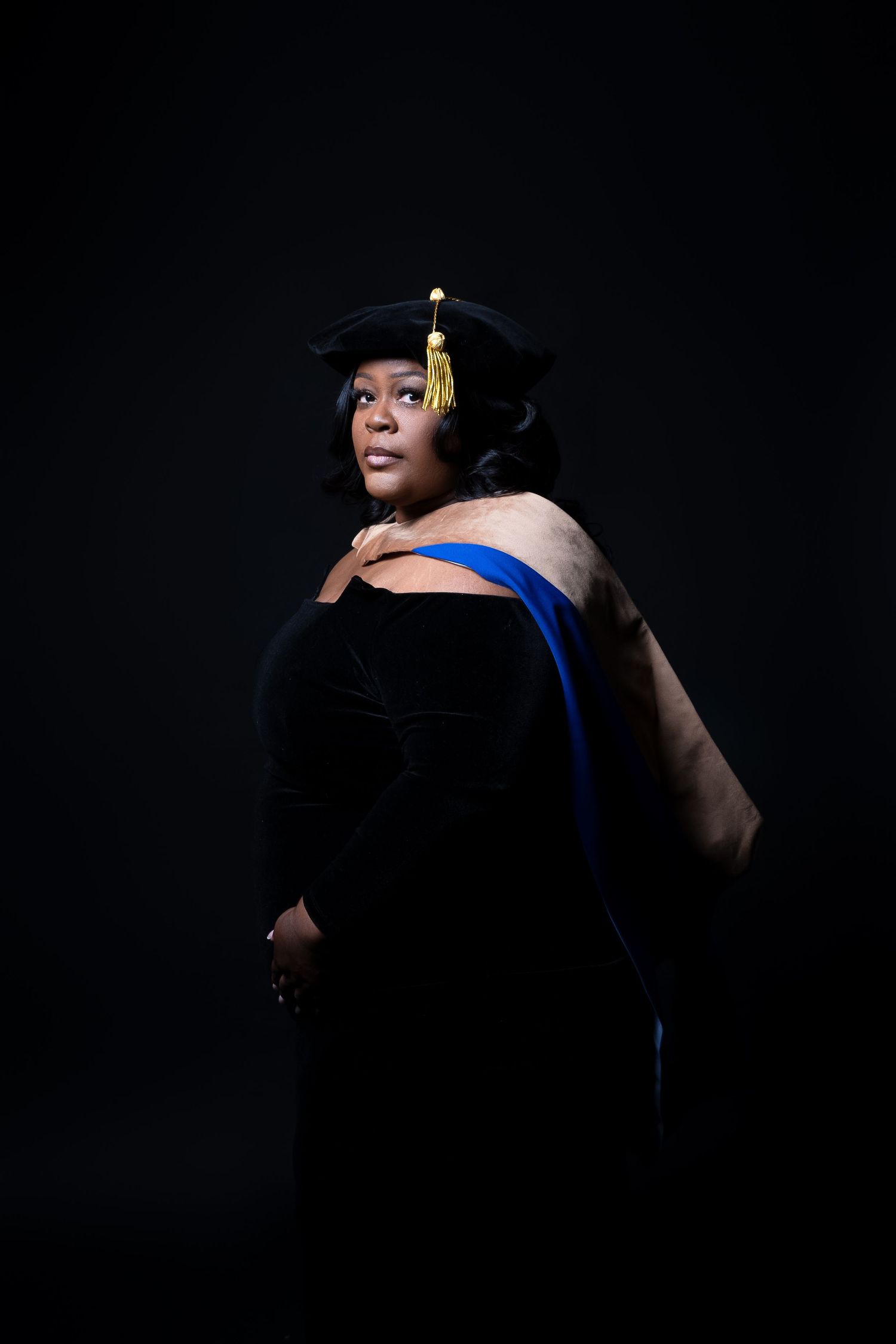Artistic graduation portrait with academic regalia against black background.