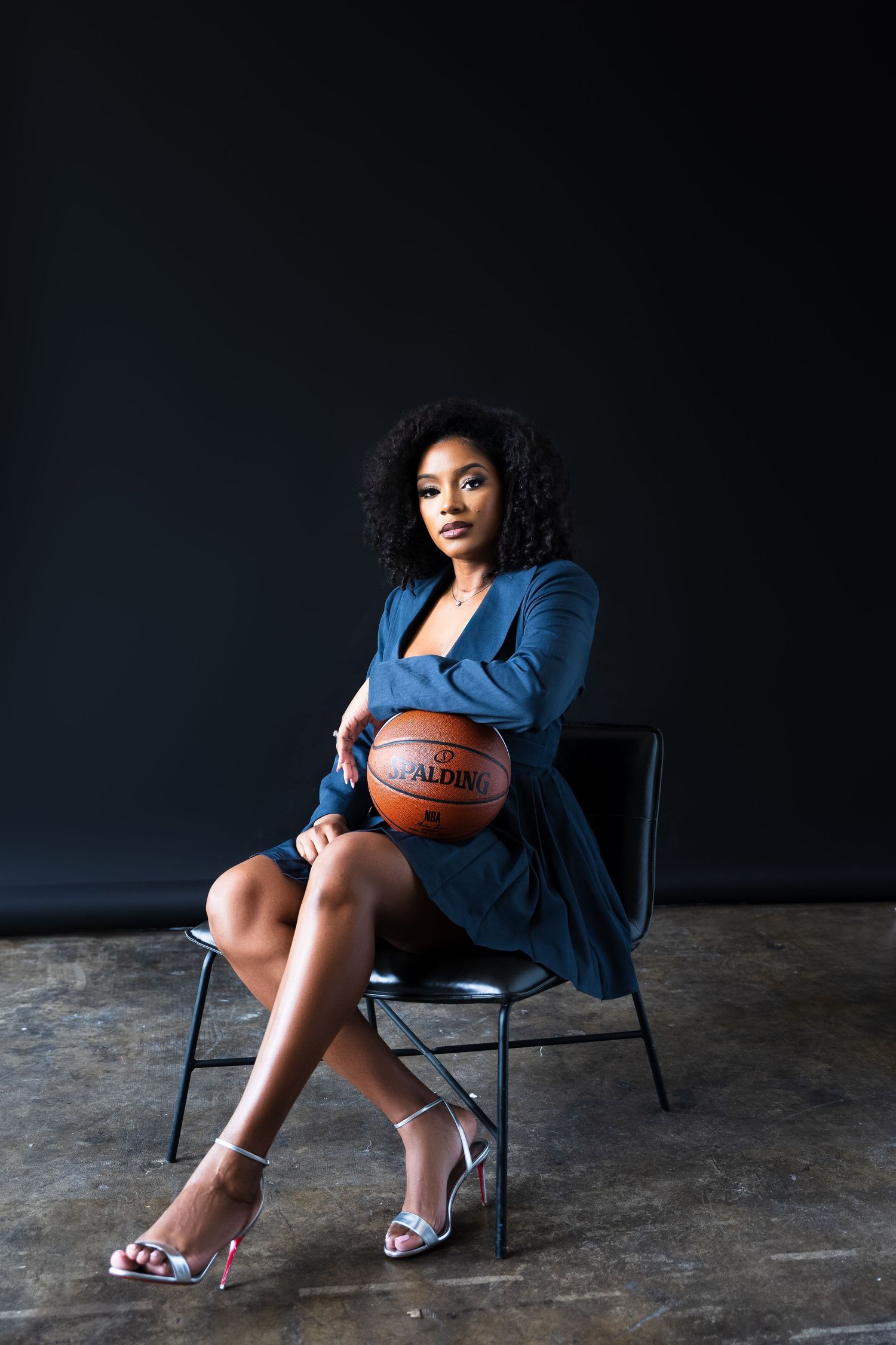 Dramatic photoshoot with blue blazer and basketball prop in dark studio setting.