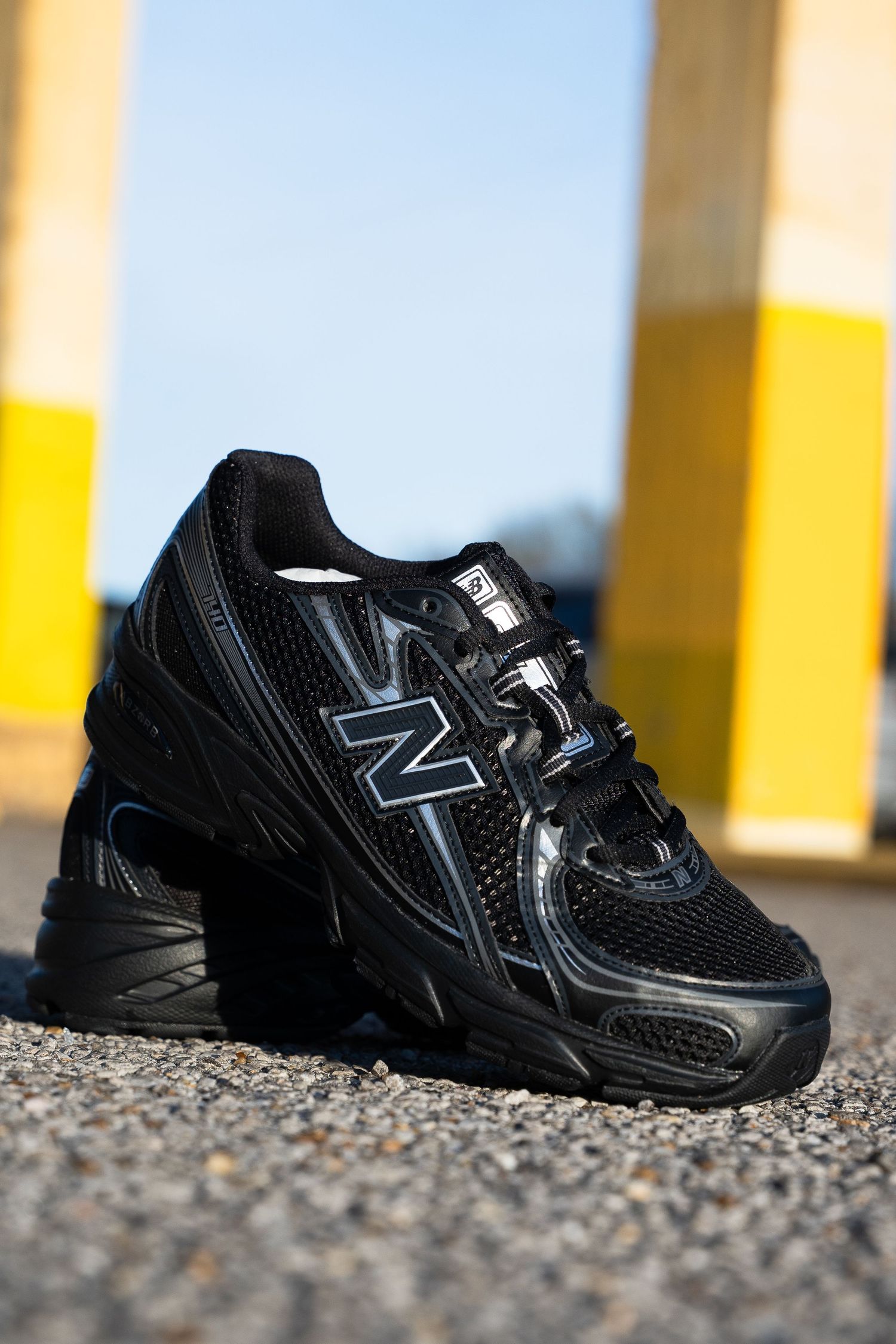 All-black New Balance running shoes photographed against yellow and white architectural elements.