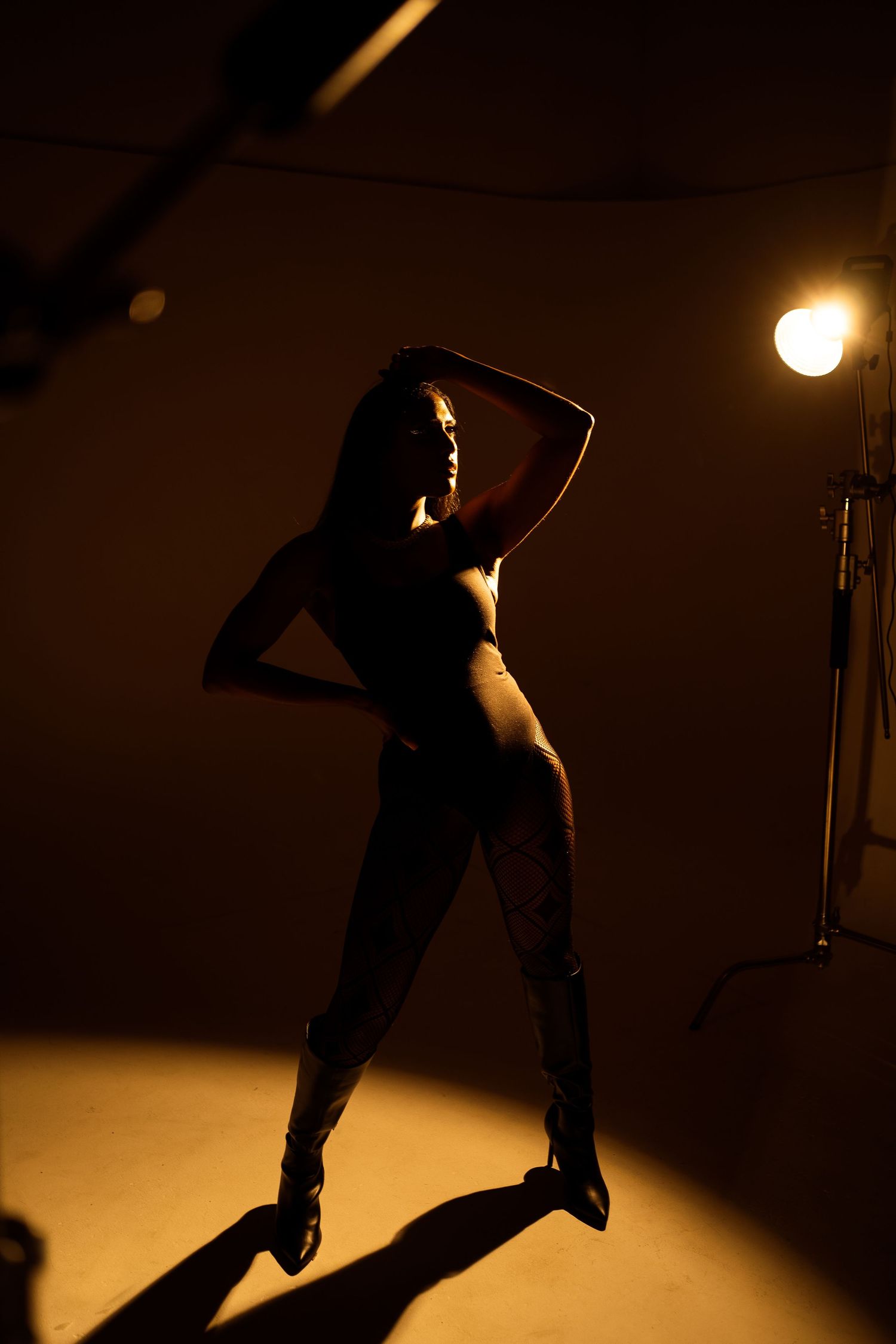 Dramatic silhouette pose in spotlight with strong shadow casting.