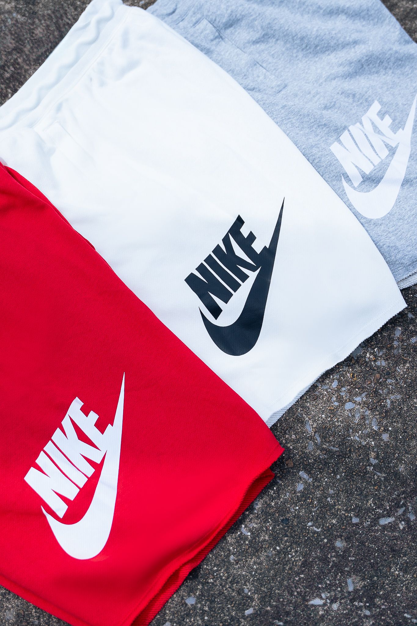 Nike logo shorts in red, white and grey colors arranged on concrete surface.