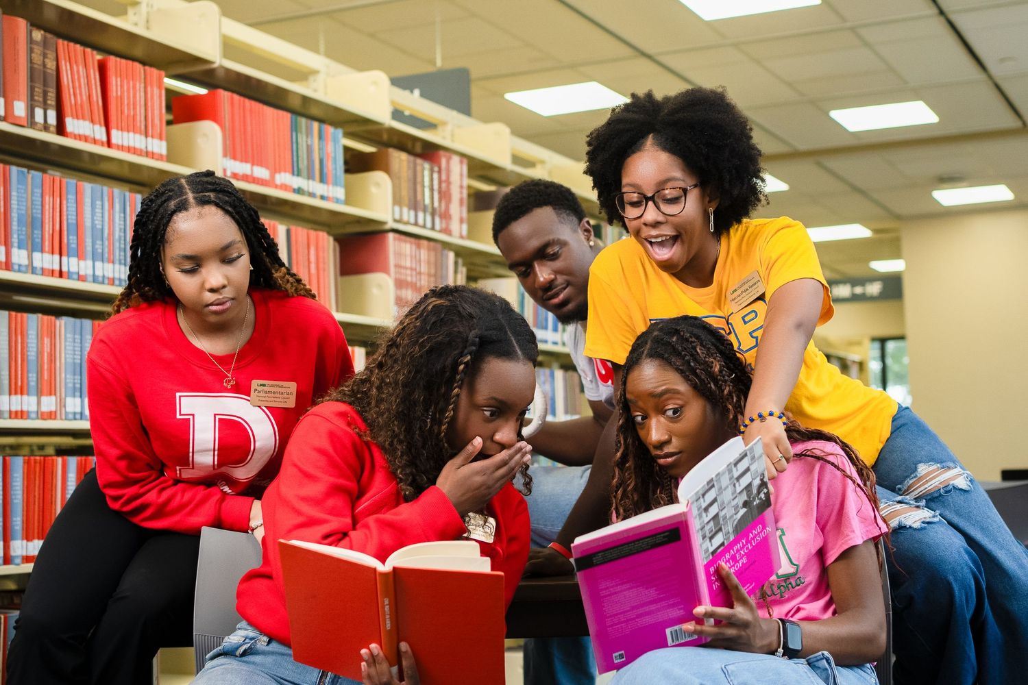 Students studying together in library with books and engaged discussion.