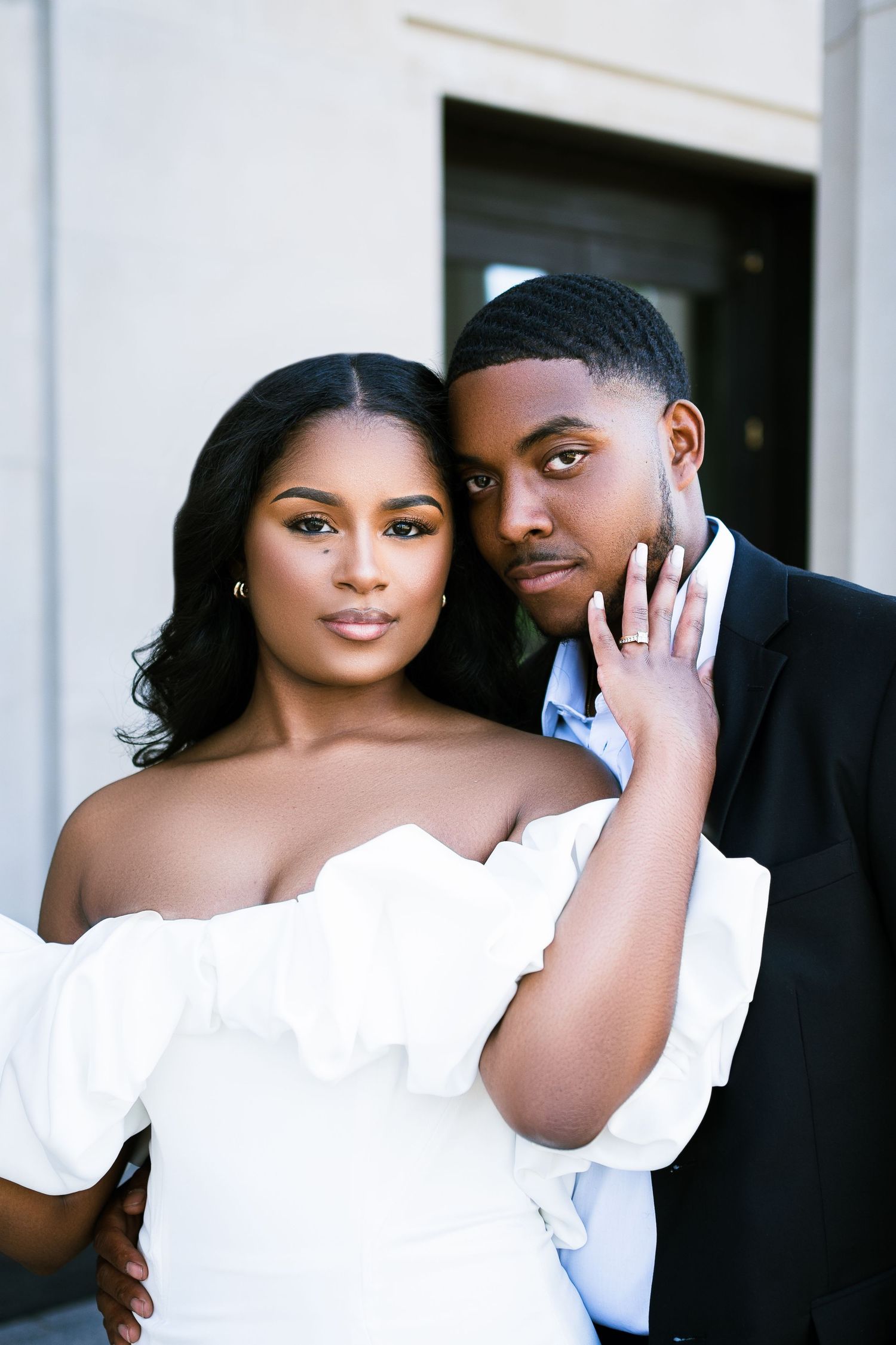 A romantic couple share an intimate moment in formal attire against a light background.