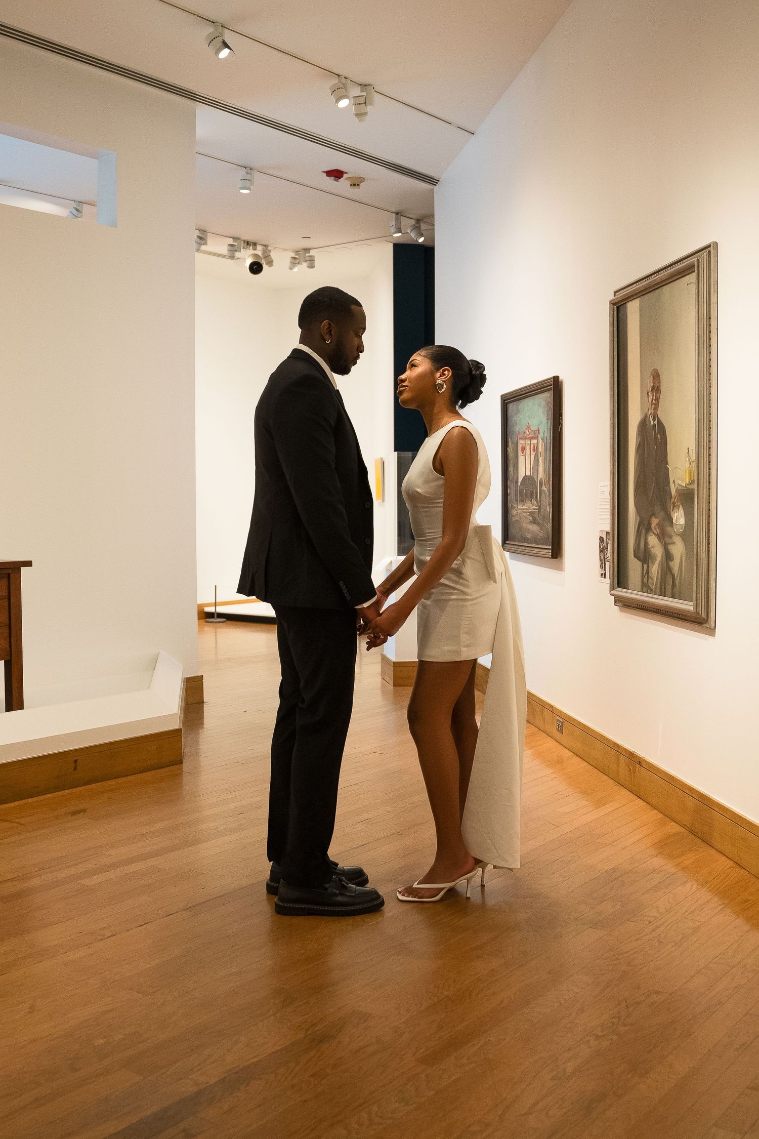Intimate moment between couple in formal wear at art gallery with white walls.