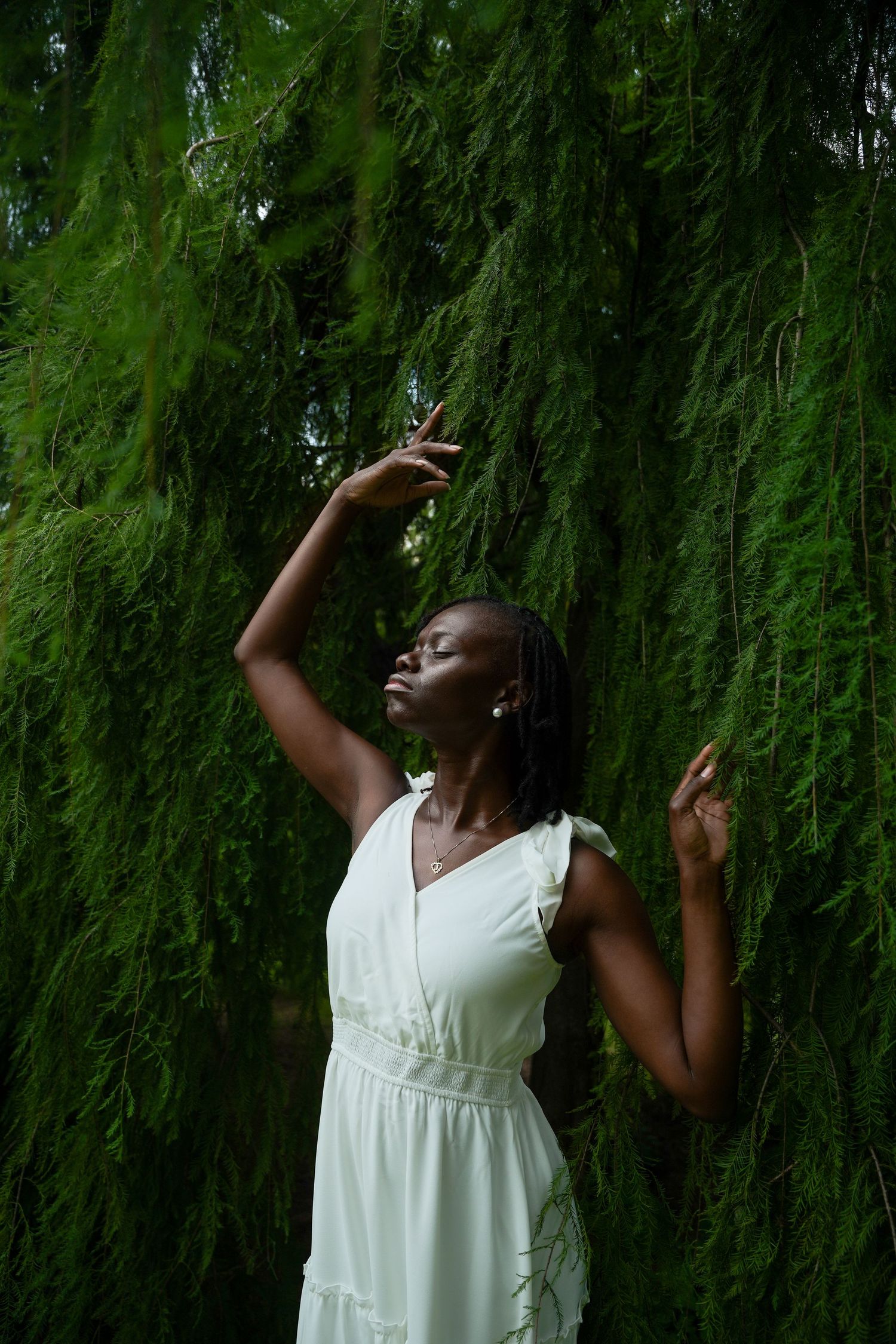 A graceful figure in a flowing white dress poses expressively against a backdrop of cascading willow branches.