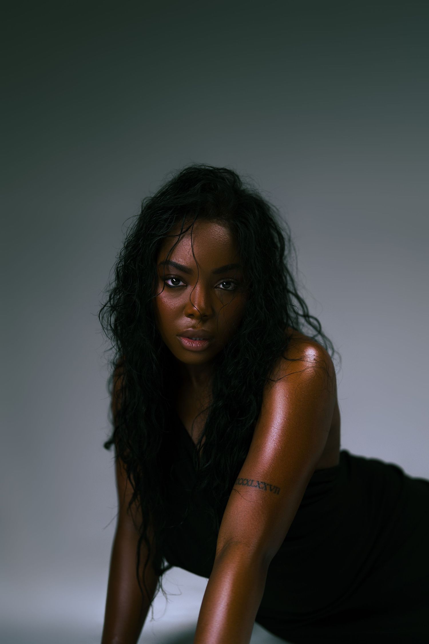 A dramatic portrait series of a person with long dark hair posing against a moody gray backdrop in black attire.