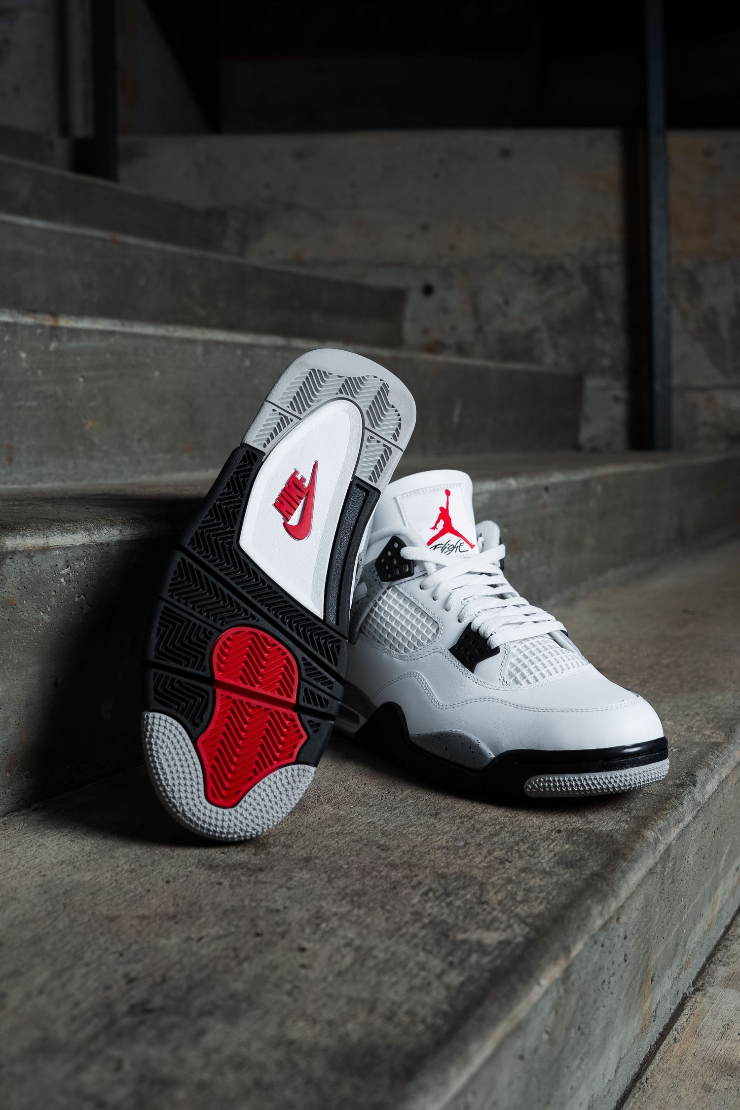 White and red Air Jordan sneakers displayed on concrete steps with dramatic lighting.