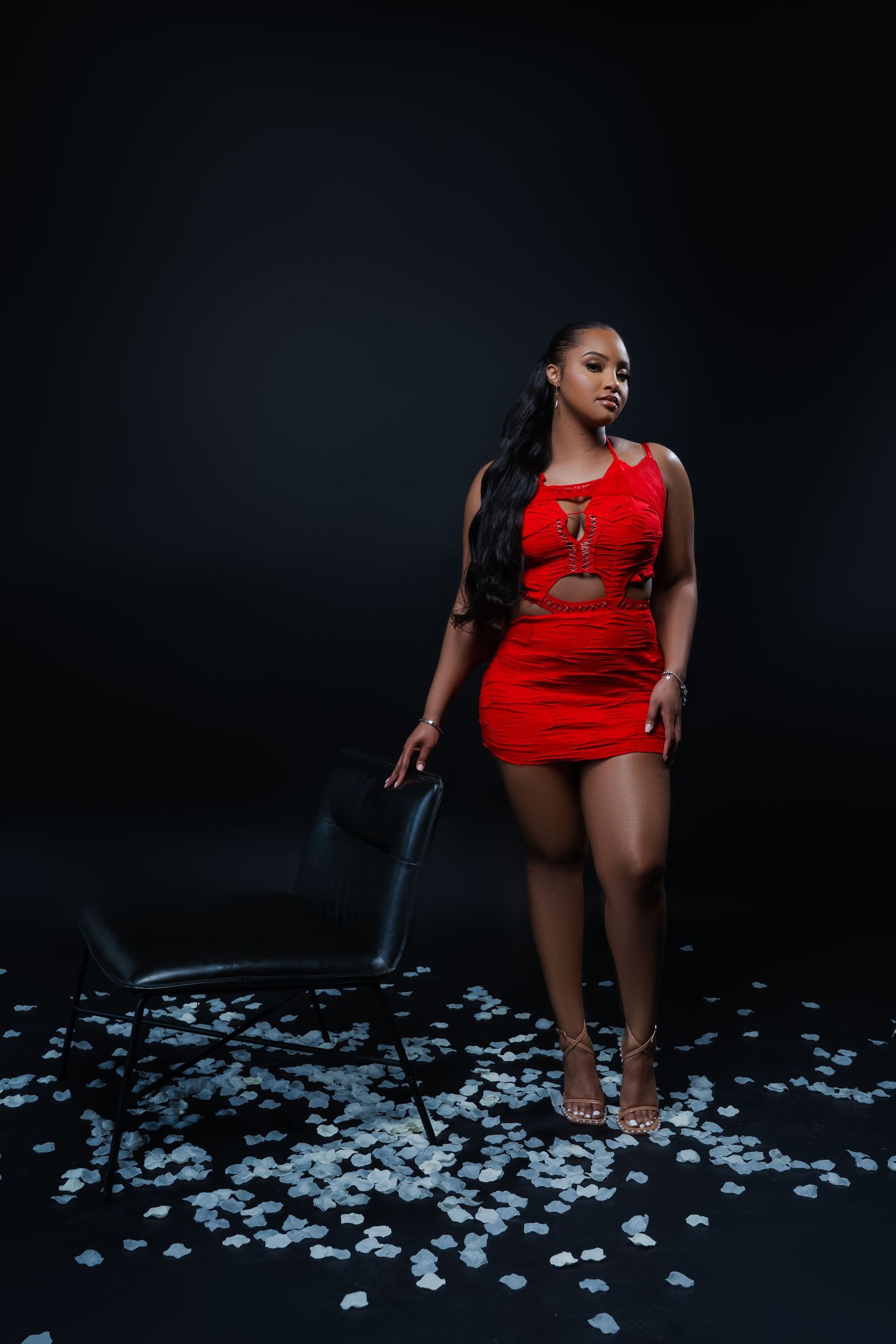 A figure in a red dress posed dramatically against scattered white flower petals on a dark floor.
