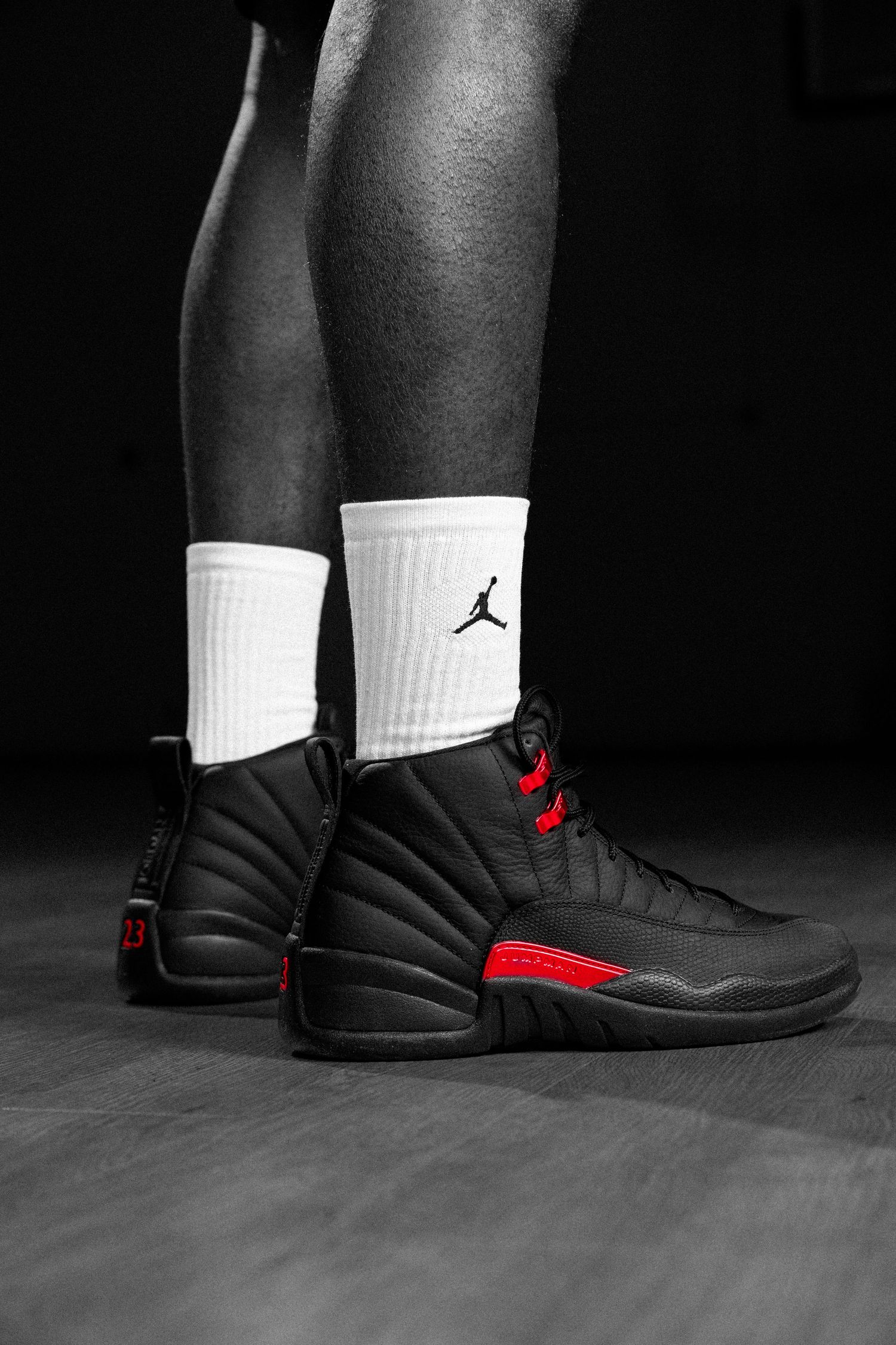 Air Jordan 12 Retro black and red sneakers worn with white Jumpman socks on a dark background.