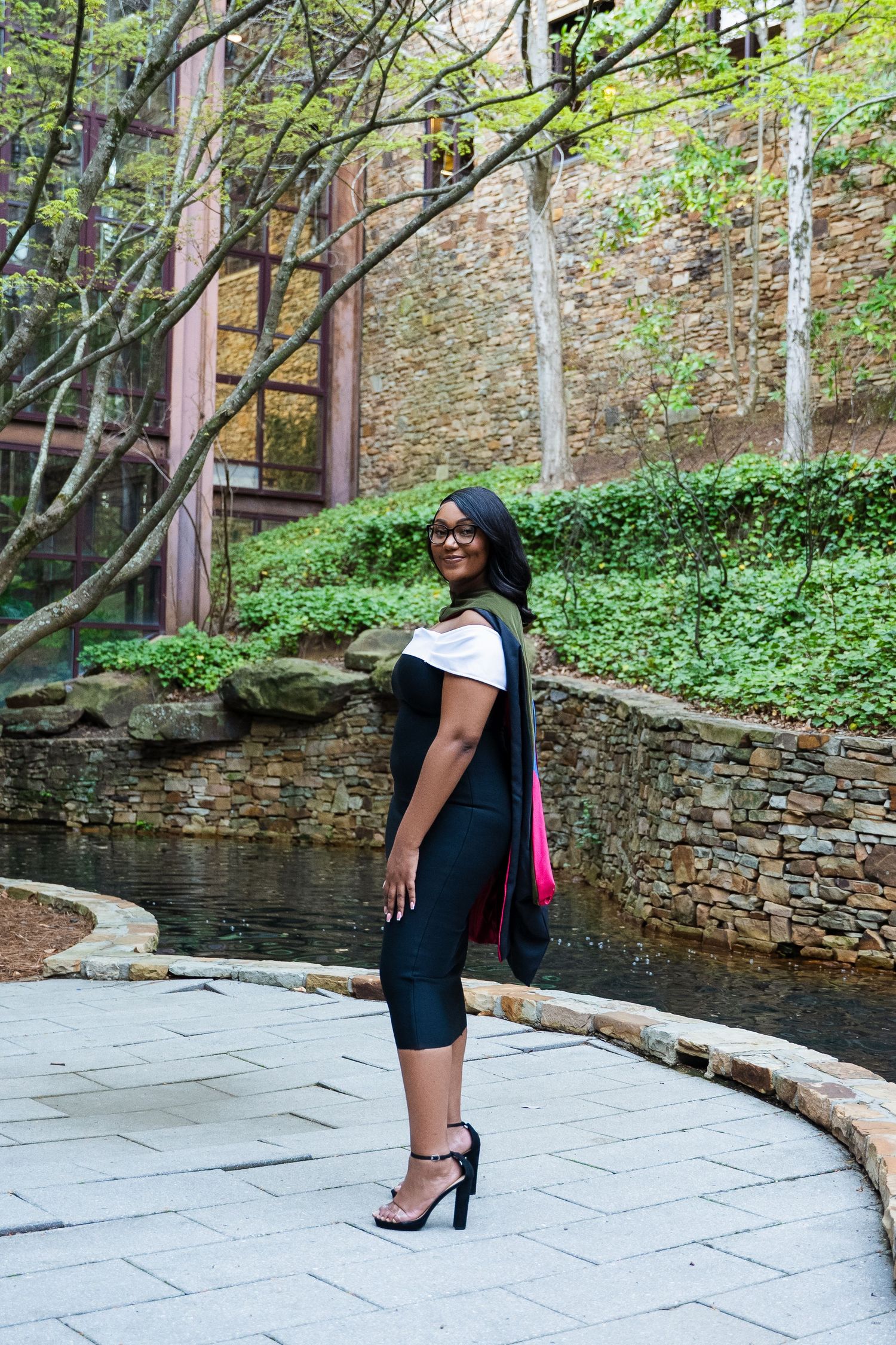 Fashionable black dress photographed against a stone wall garden setting with curved pathway.