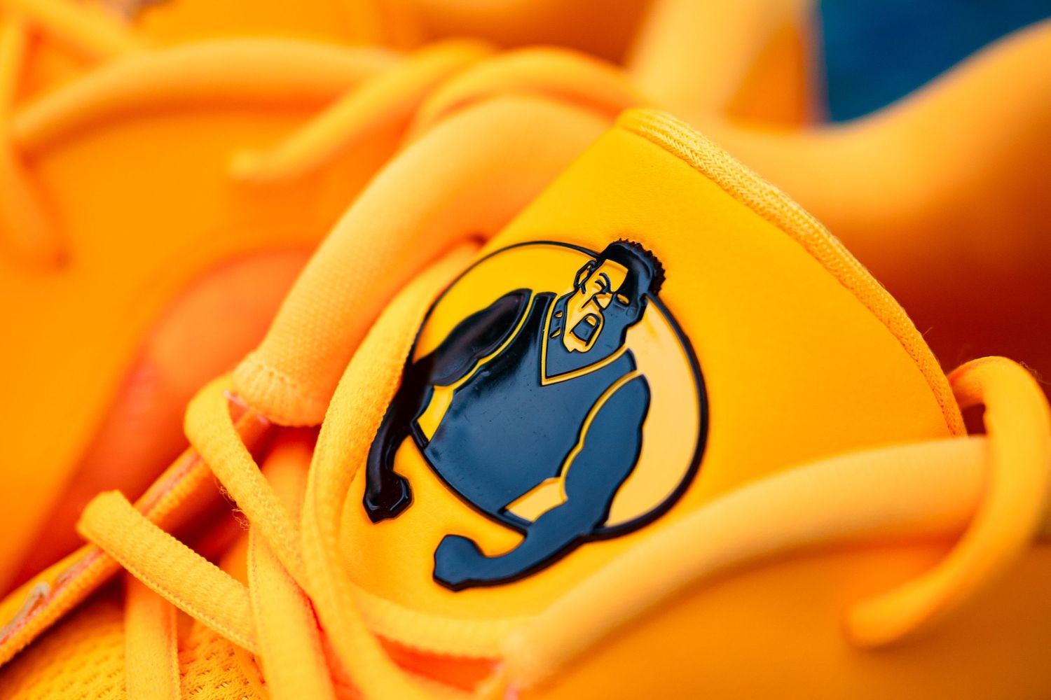 Macro detail shot of yellow sneaker showing blue circular logo emblem.