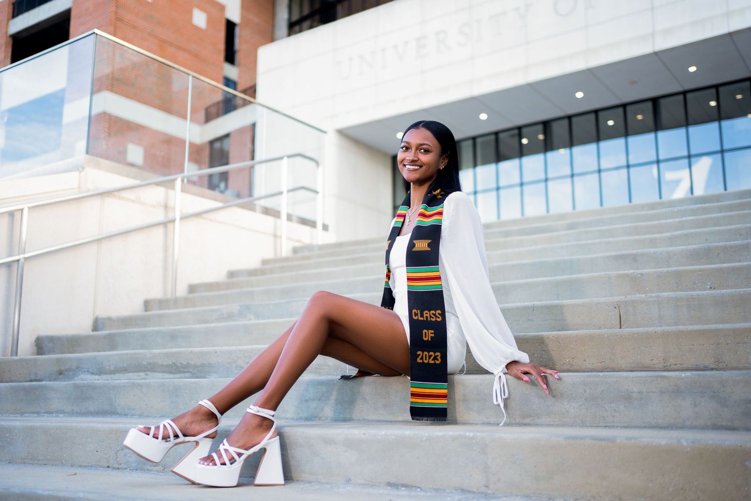 Graduate posing on concrete steps in formal attire and graduation regalia.
