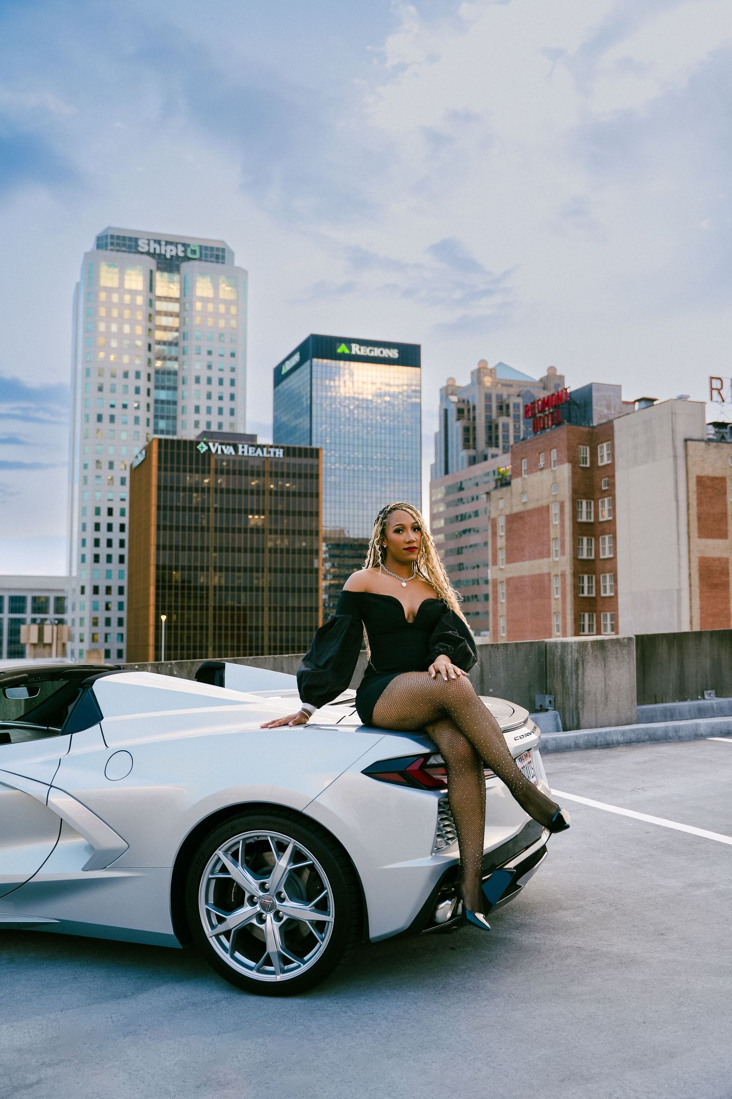 A white McLaren sports car parked on a rooftop parking lot with city buildings in the background.
