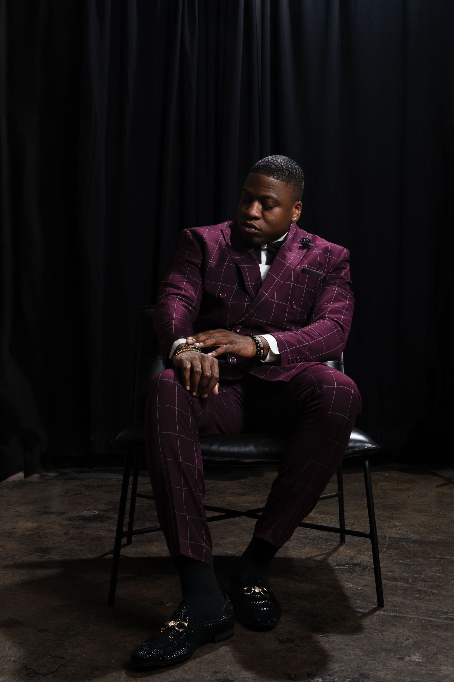 Dramatic portrait in burgundy plaid suit against dark studio background.