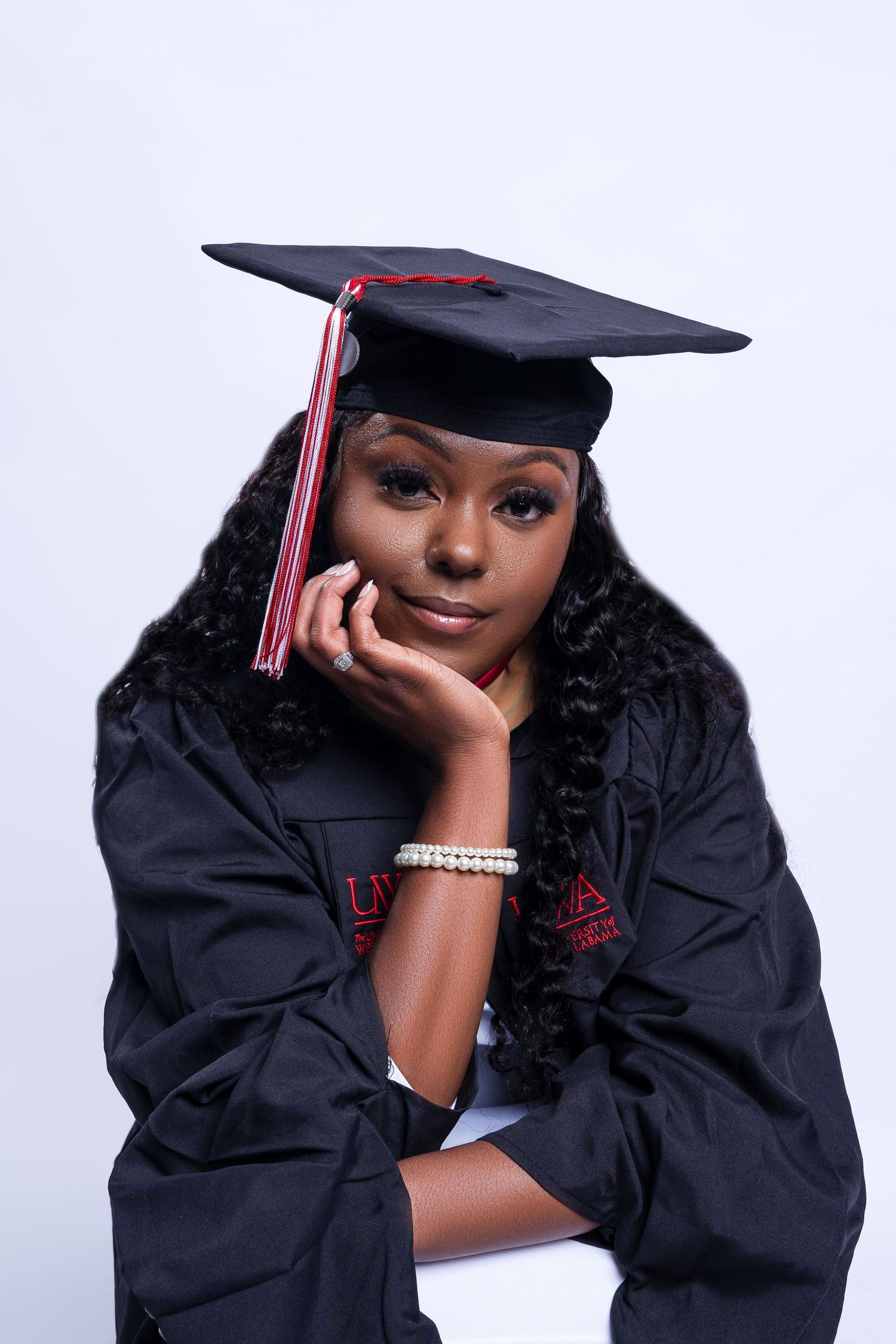 Graduate in traditional black cap and gown poses for formal portrait against white background.