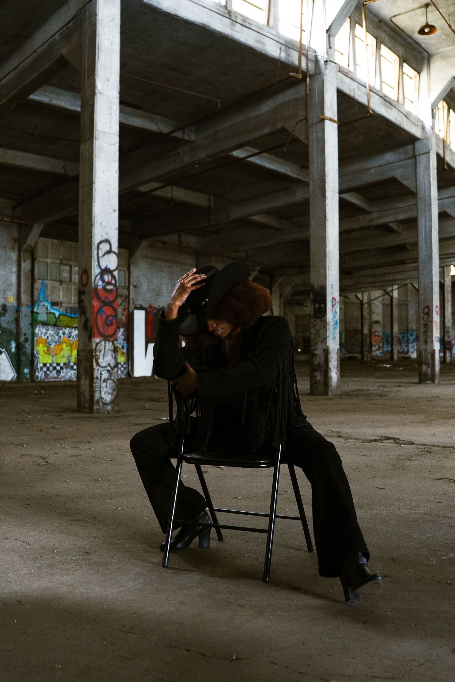 Silhouette of person sitting on folding chair in abandoned industrial space.
