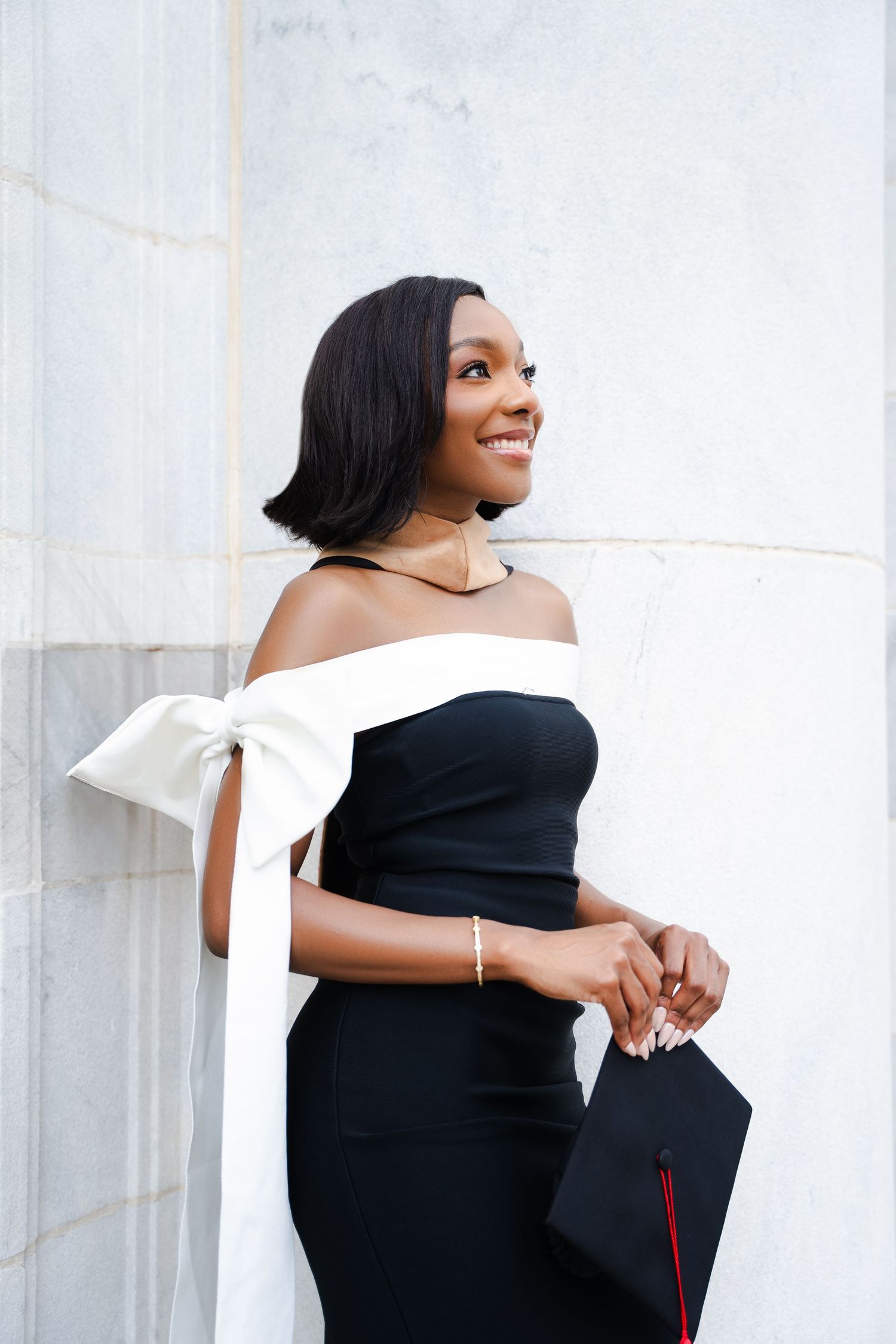 Portrait against white wall wearing black and white formal dress with bow detail.