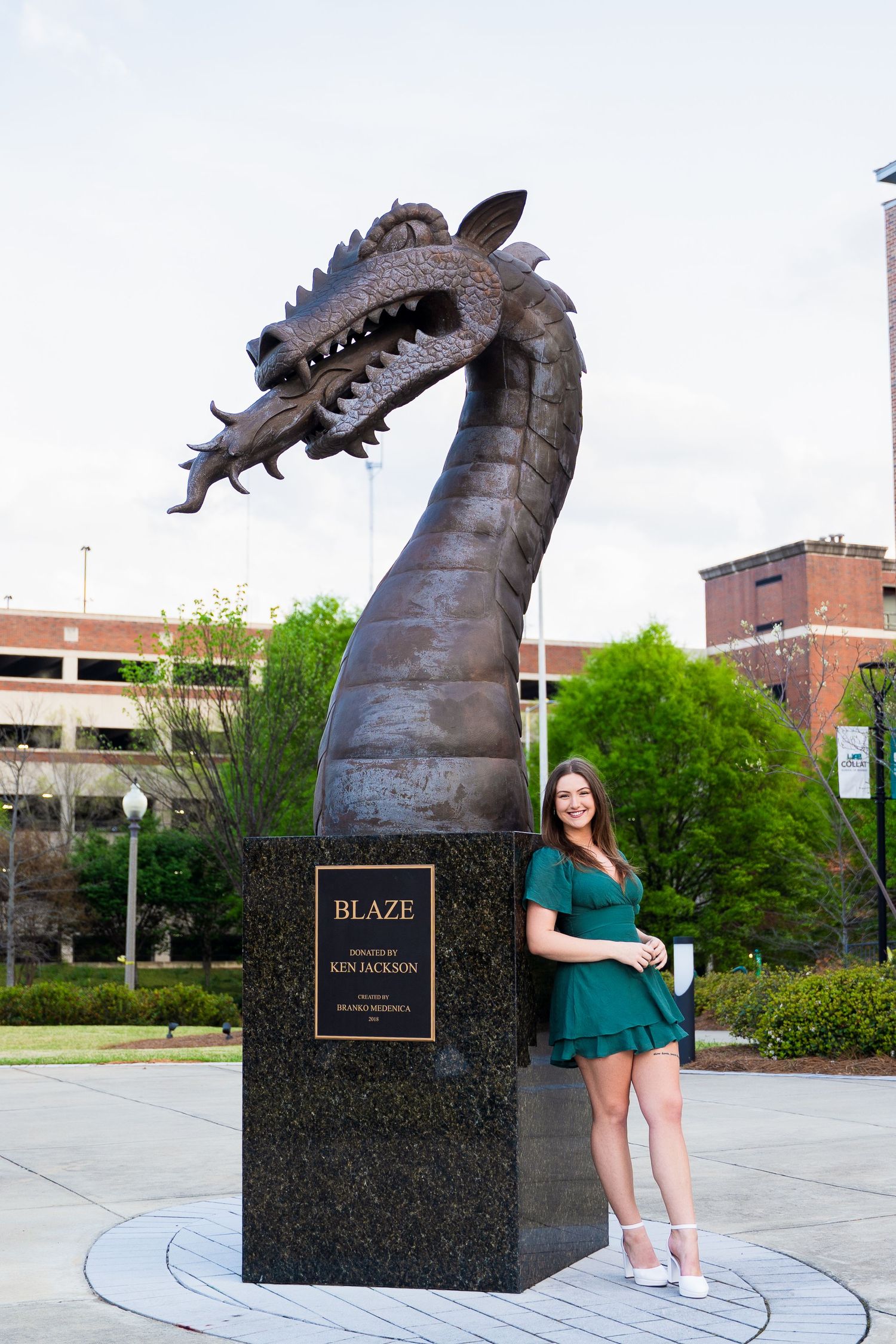 Graduate poses next to large dragon sculpture called Blaze on campus.