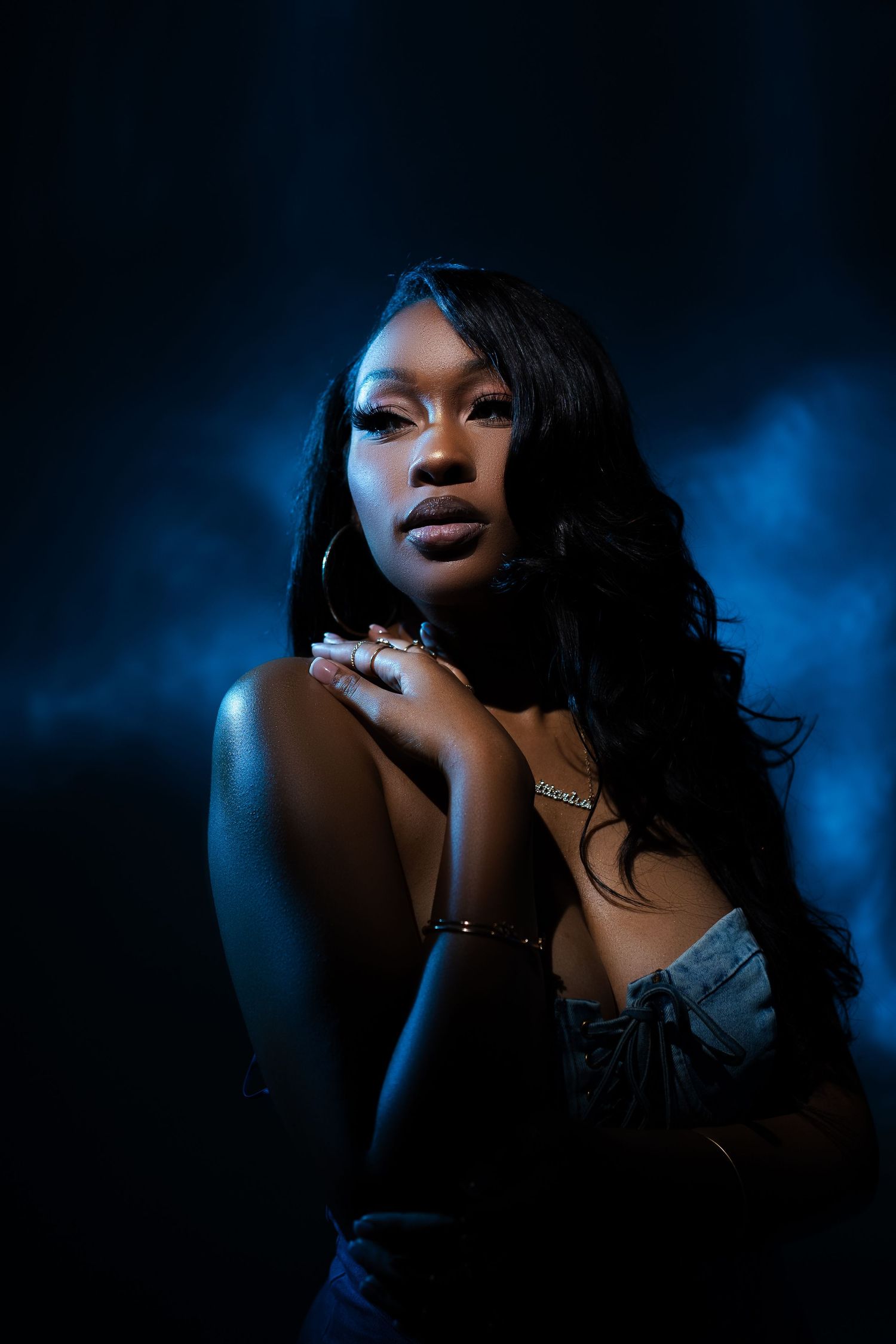 A dramatic portrait series in blue lighting shows a figure with dark hair and jewelry against a moody dark background.