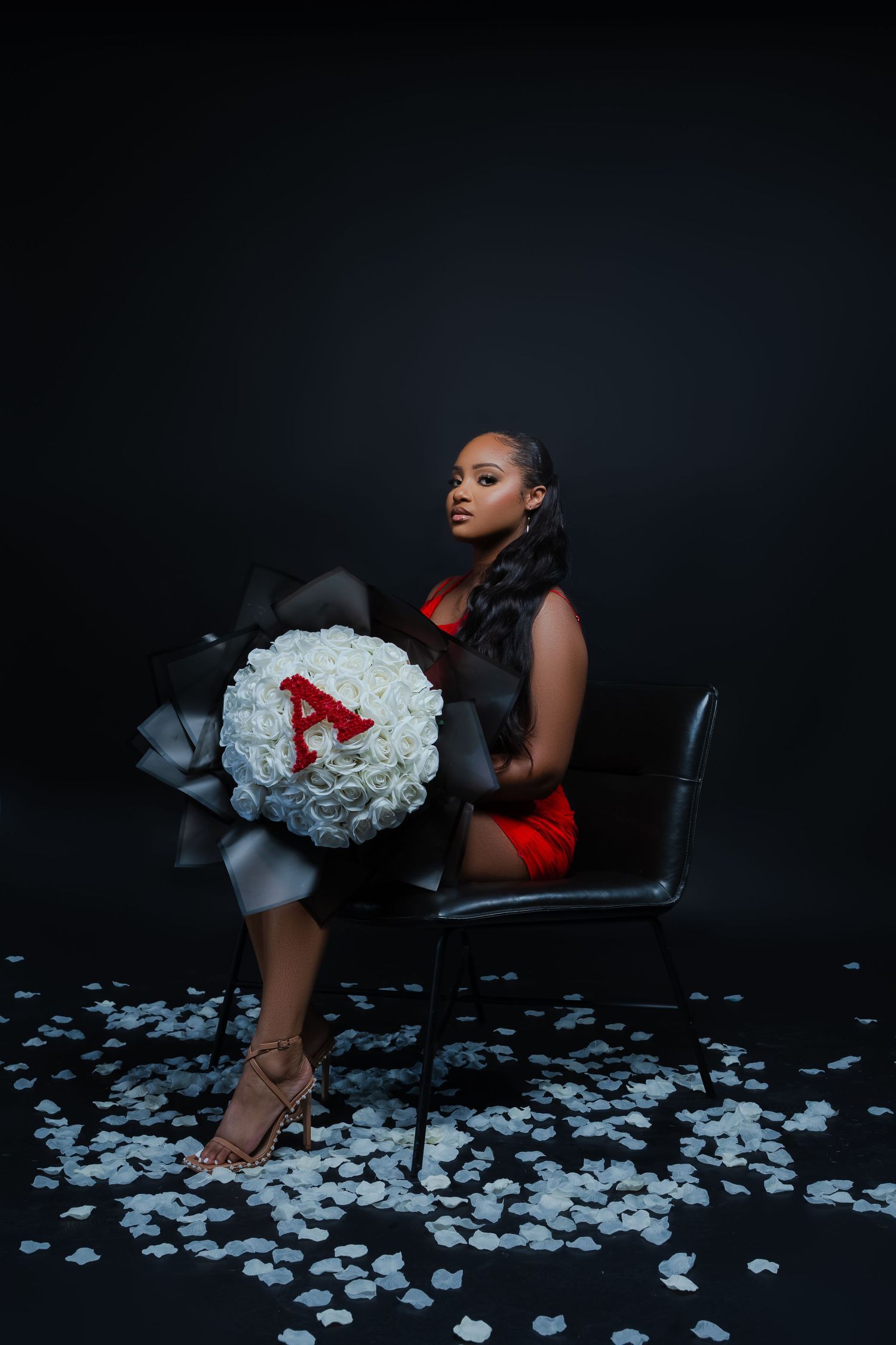 Artistic portrait with white flowers scattered on dark floor around a leather chair.
