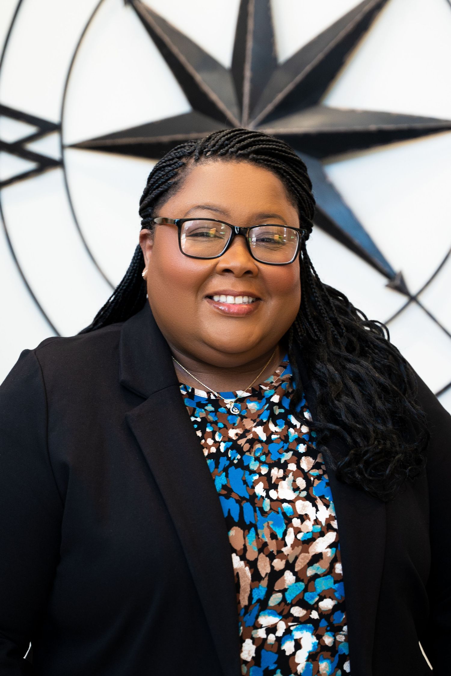 Professional headshot against star wall background wearing patterned blouse and blazer.