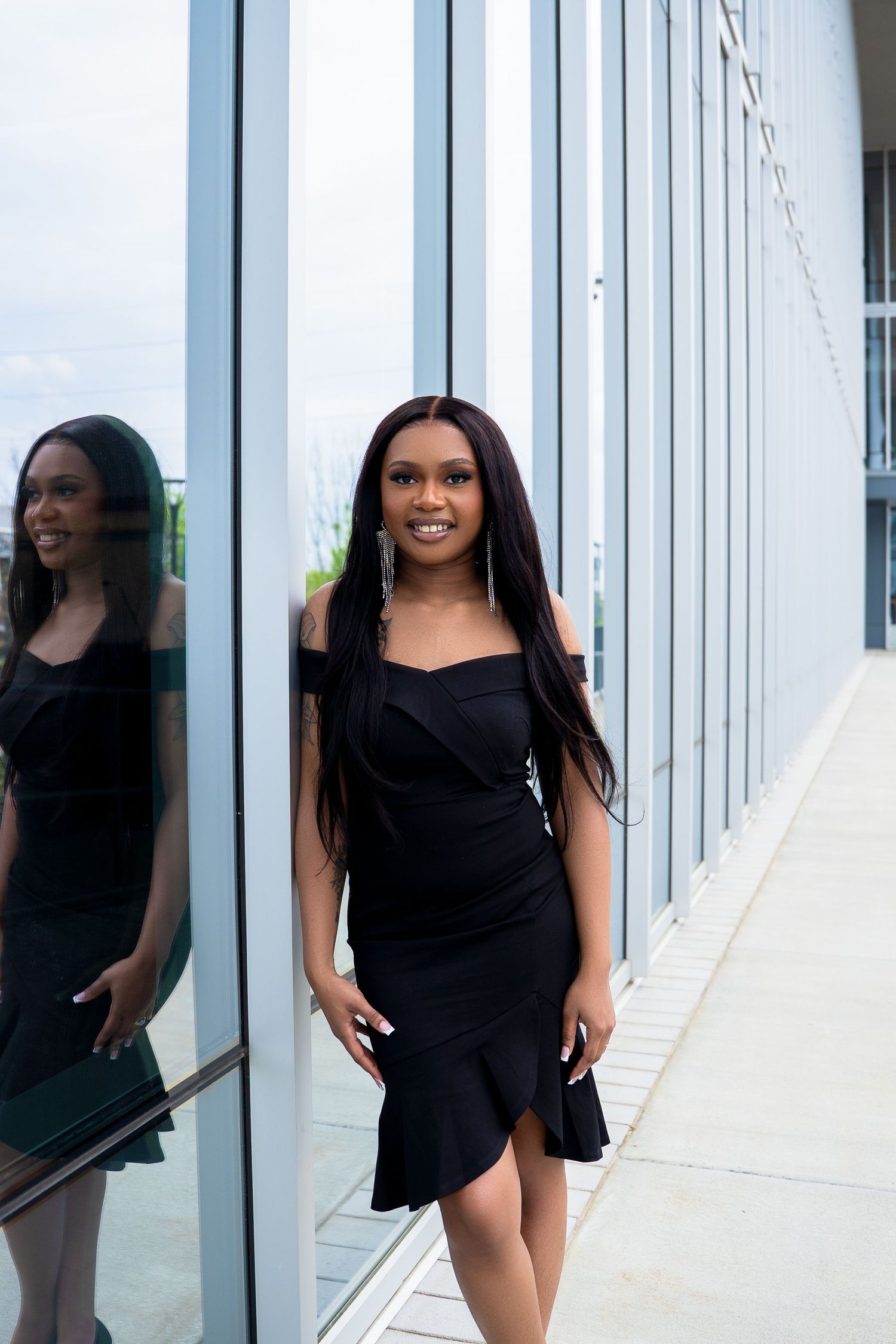 Person in black dress poses by reflective glass wall.