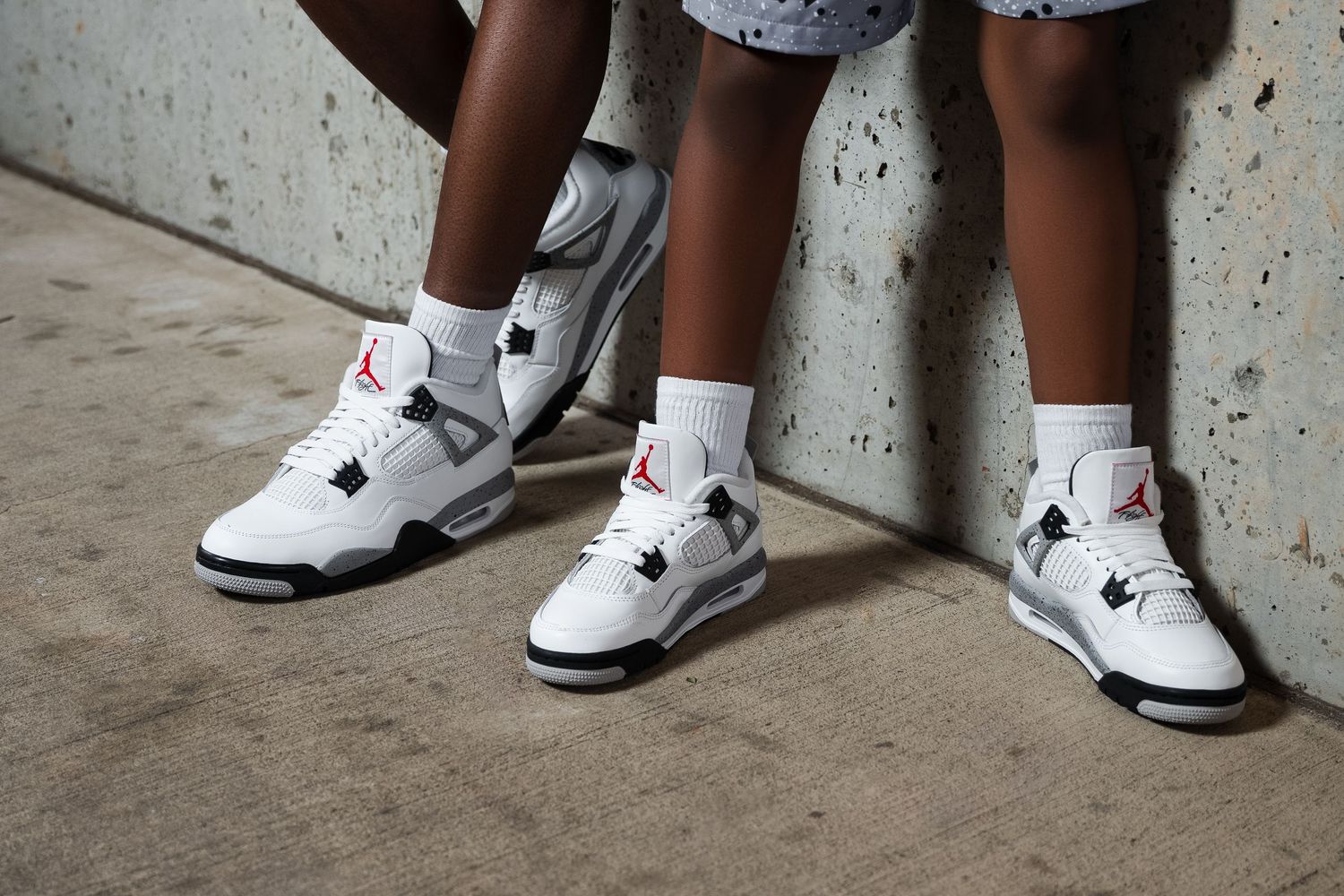 Multiple angles of white athletic shoes worn by people standing against a concrete wall.
