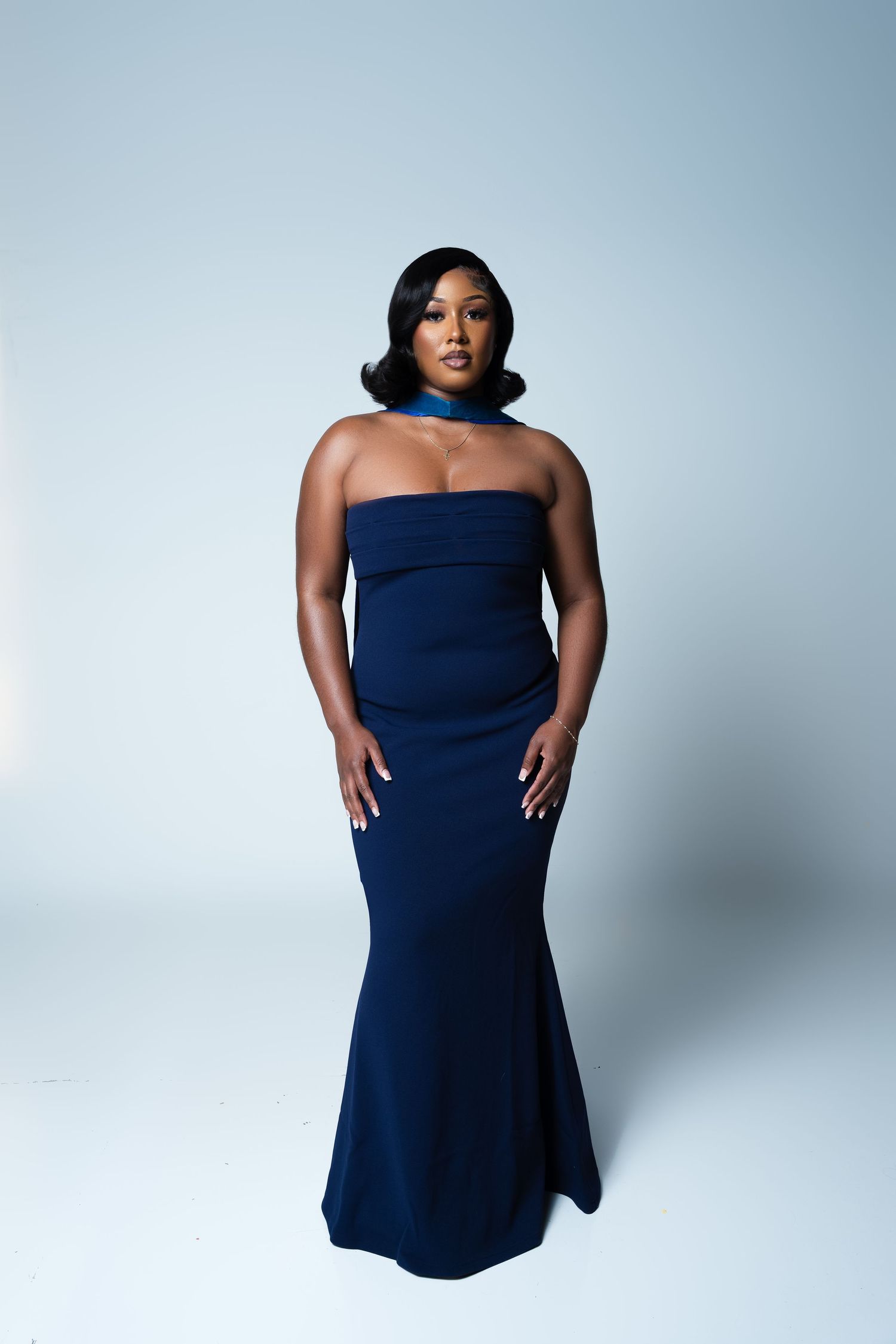 Woman in elegant navy blue strapless mermaid gown with choker necklace poses against light background.