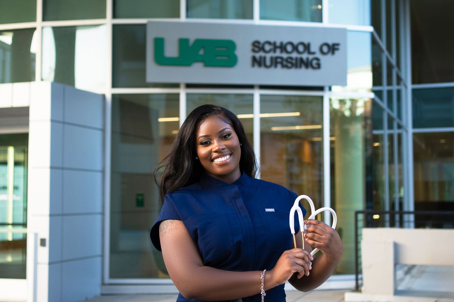 Healthcare worker in navy uniform celebrating outside nursing school.