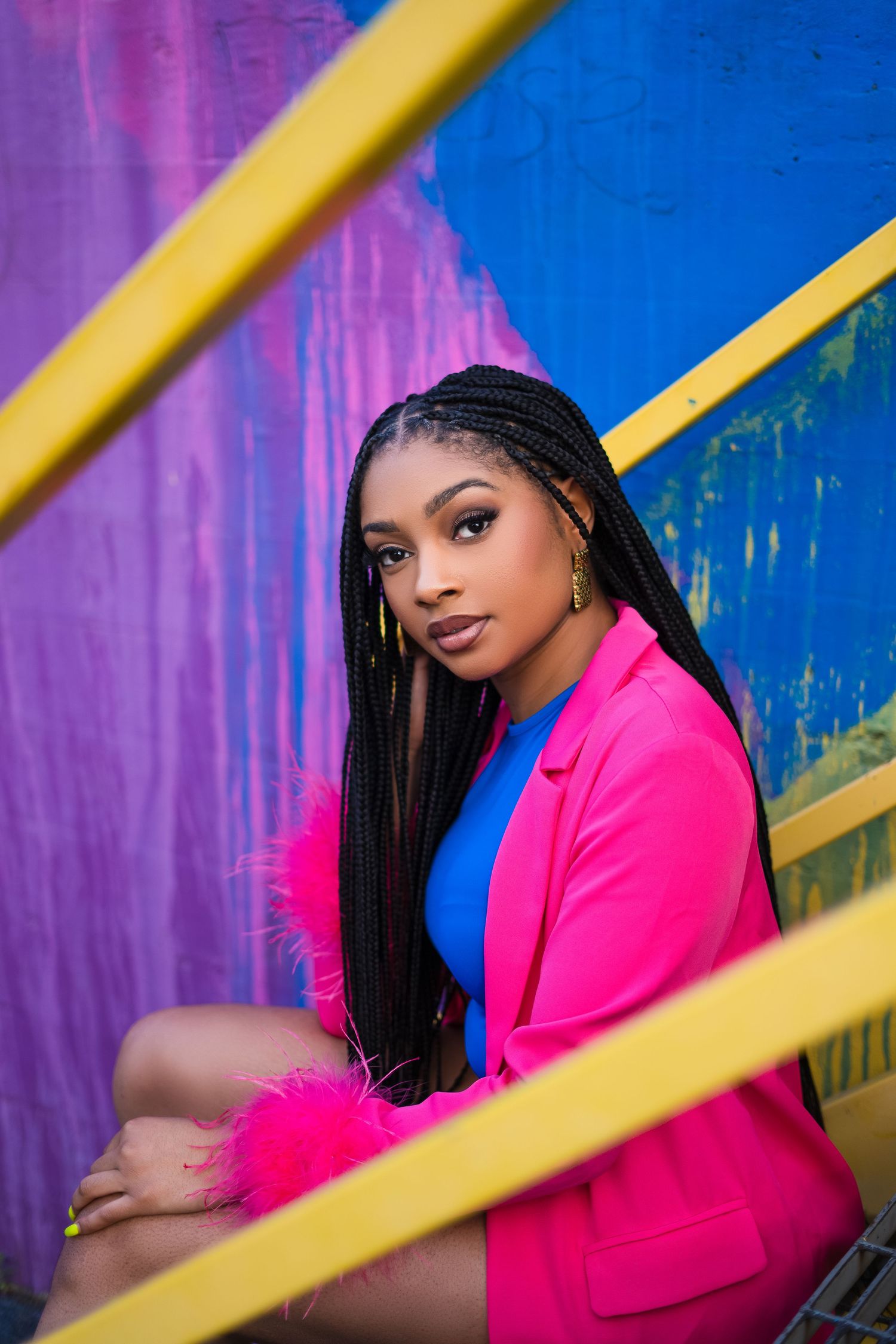 Portrait against colorful wall features pink blazer and geometric yellow framing elements.