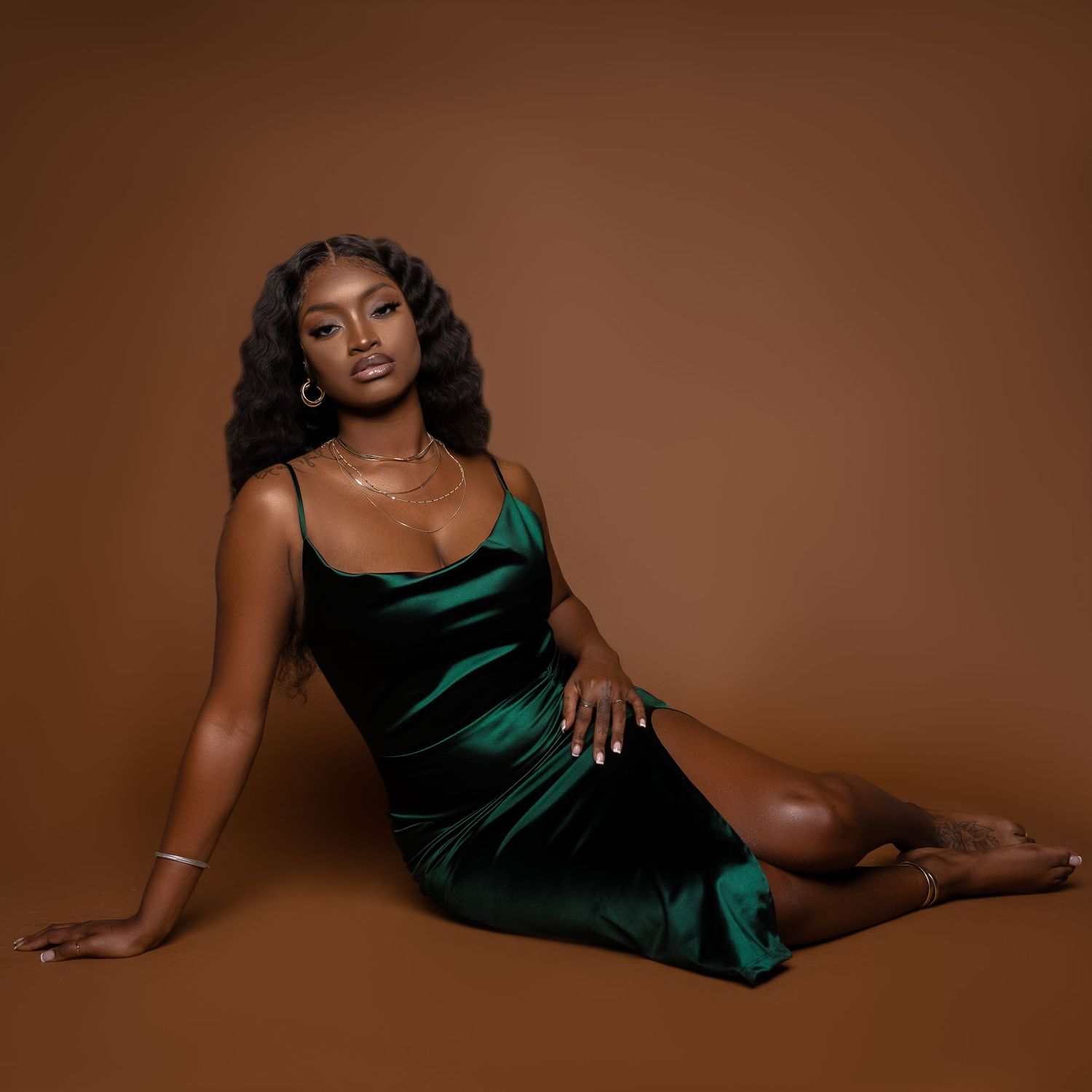 Woman in emerald velvet dress poses on brown backdrop.