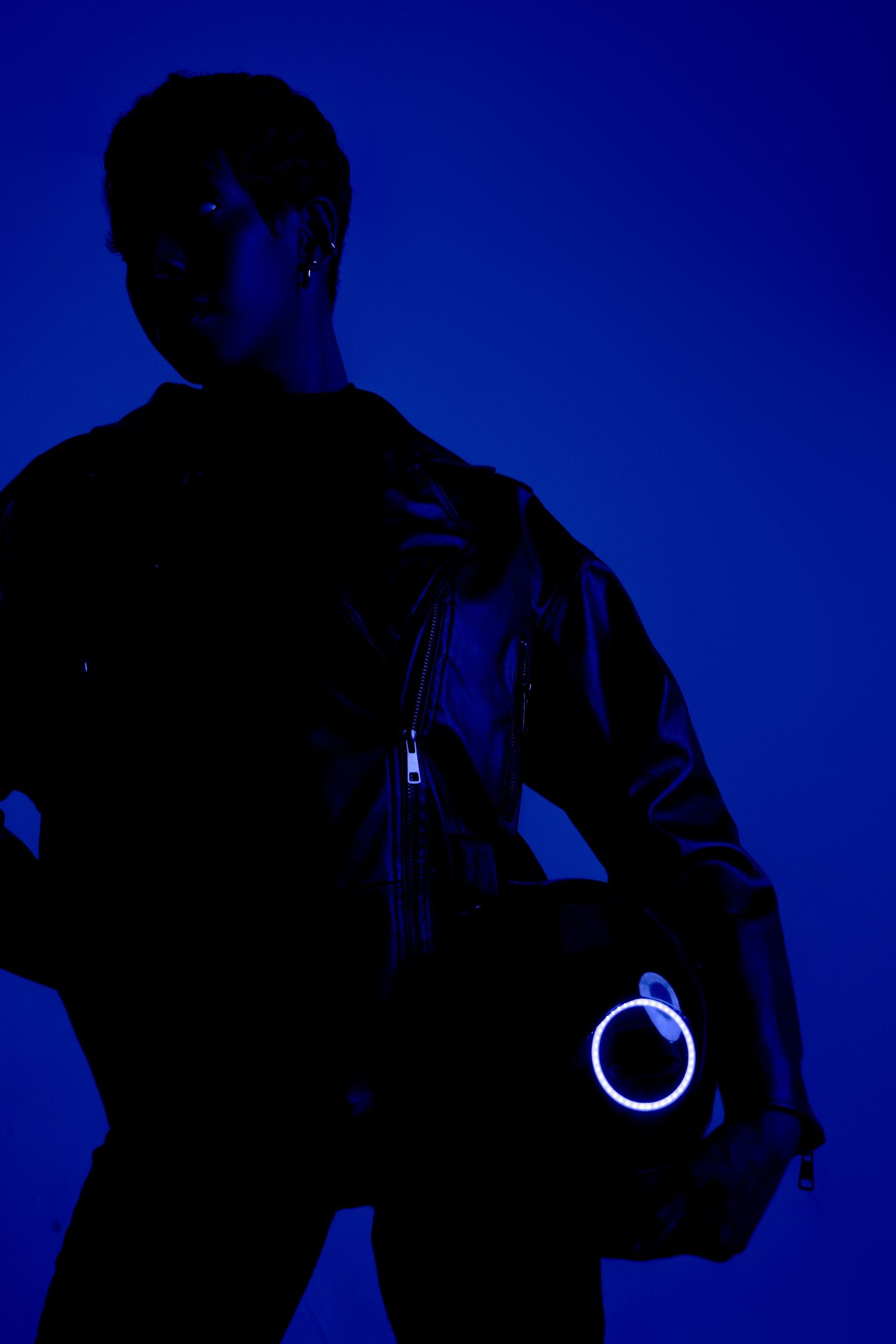 Dramatic silhouette portrait with illuminated circle accent against royal blue backdrop.