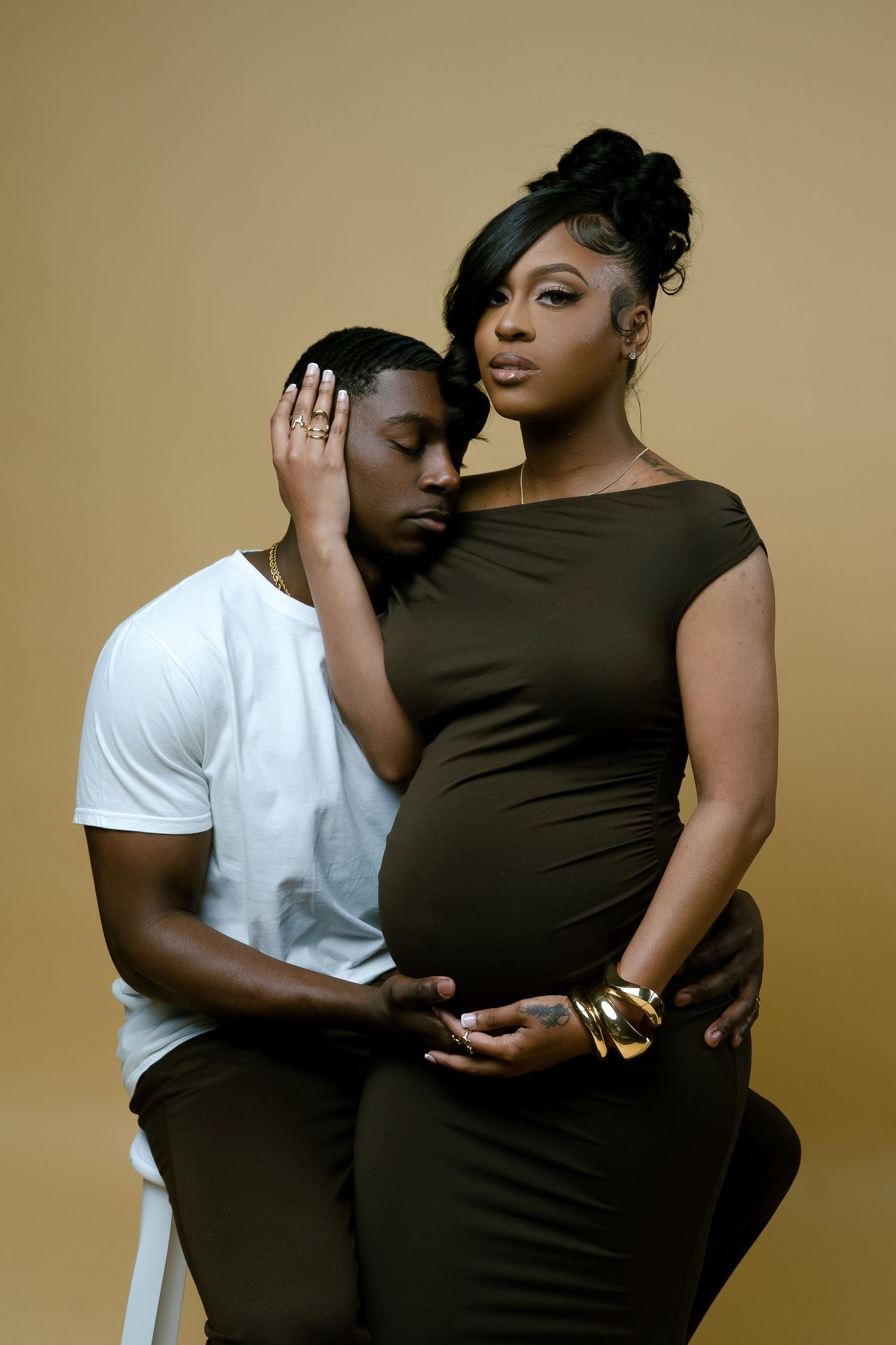 Intimate maternity portrait with couple in olive dress and white shirt against neutral background.