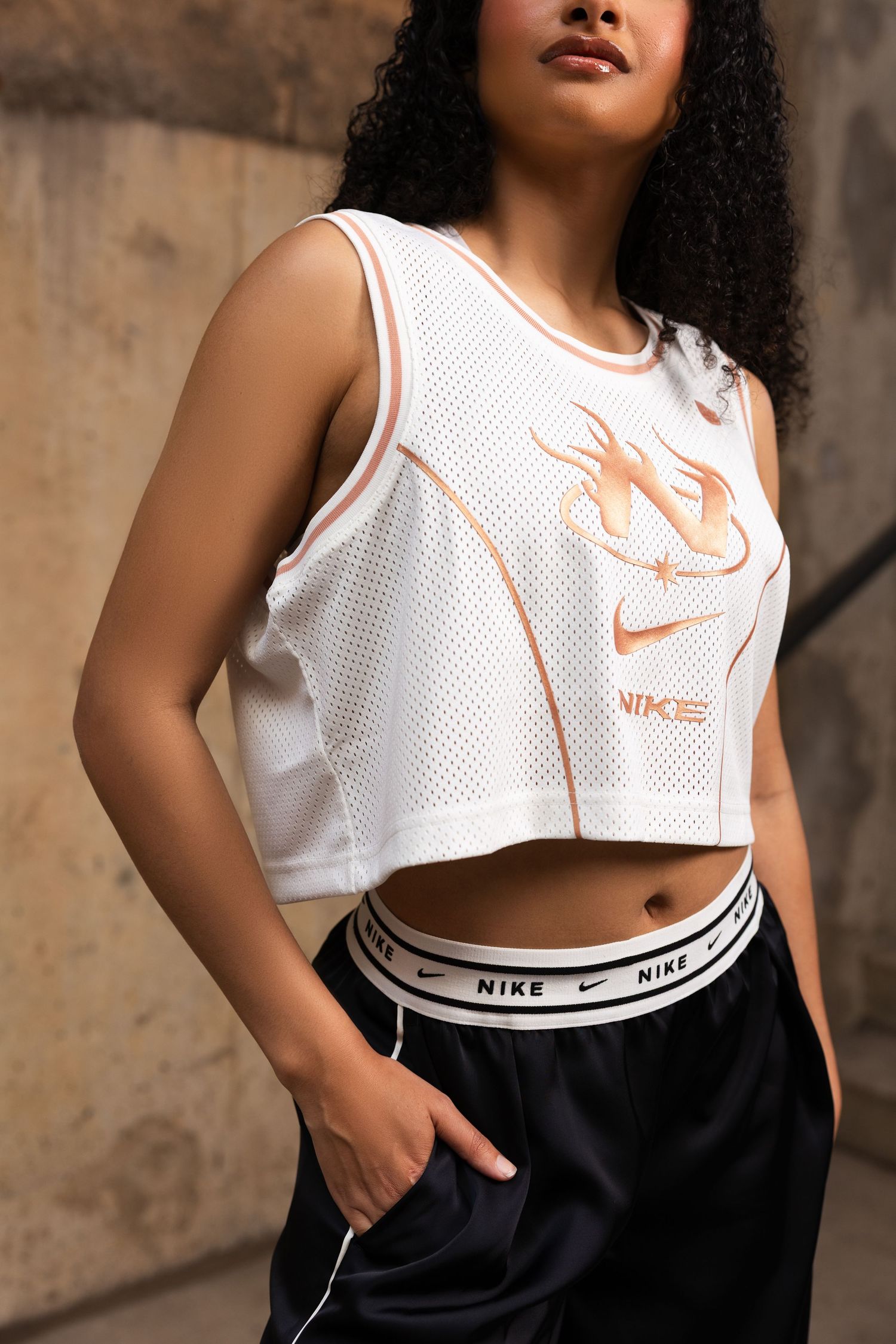 Athletic woman wearing a white Nike crop top and black shorts poses against a textured wall background.